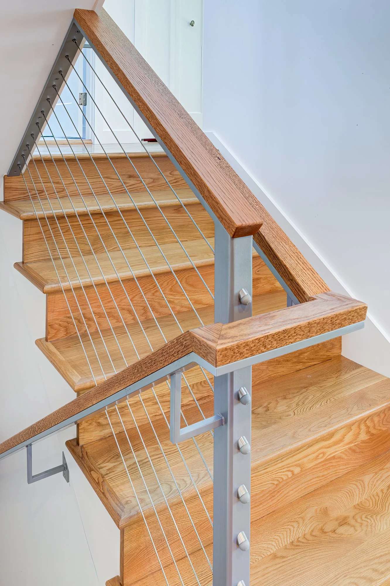 Custom stair railing with wood handrail and steel cable infill, highlighting craftsmanship and providing a modern connection between levels of the remodeled home.