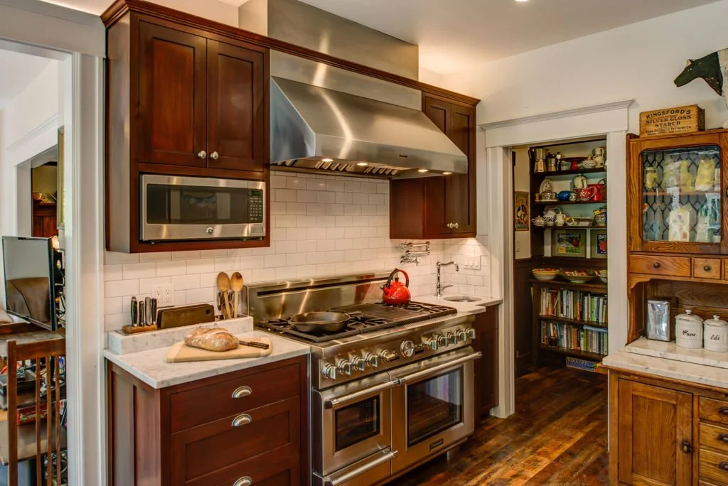 Range wall with stainless stove and hood, dark wood cabinetry, and a built-in pantry. Traditional Craftsman details pair with clean modern finishes for a warm look.