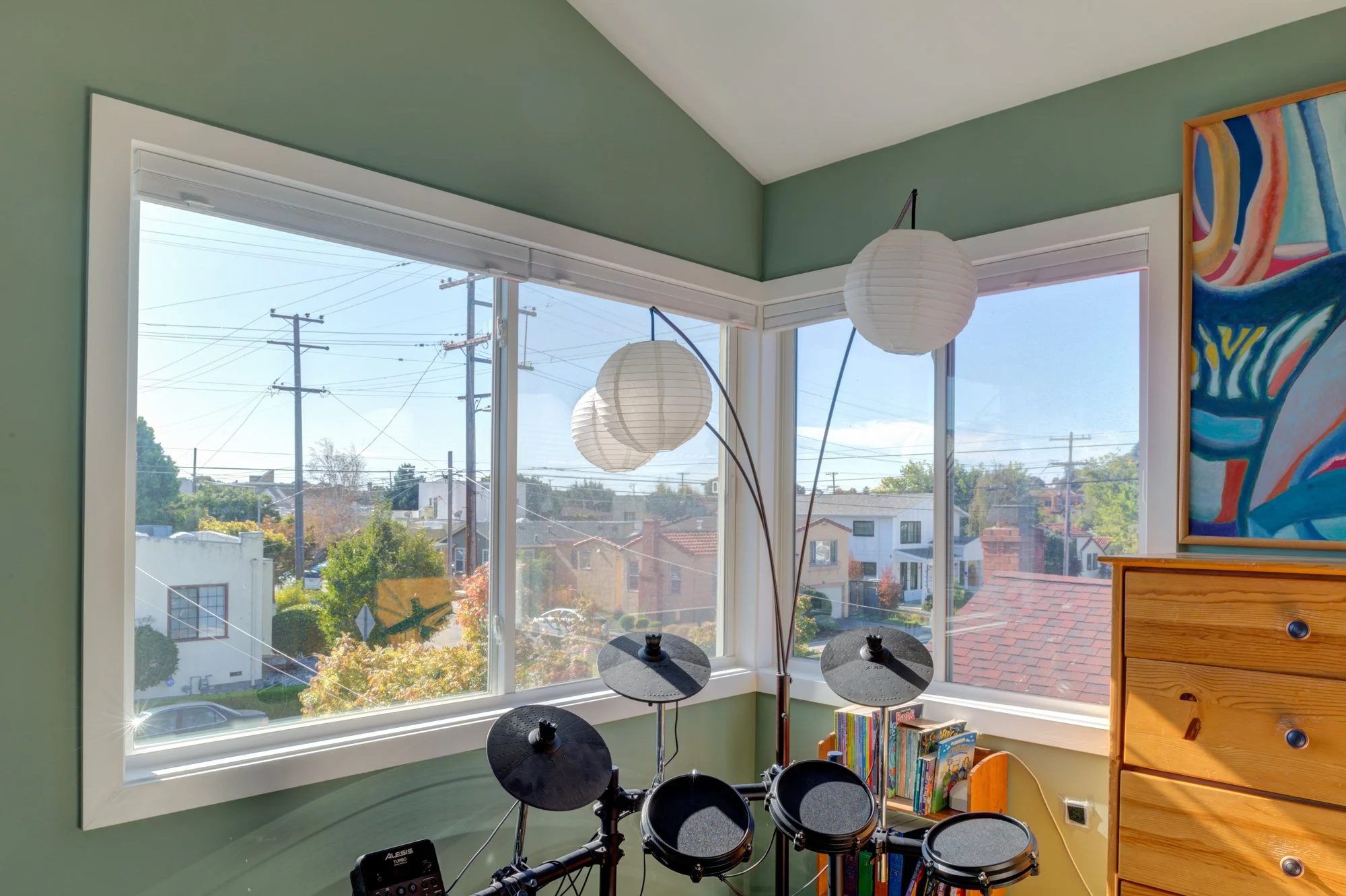 Second-story bedroom with soft green walls, large corner windows, and natural light, creating a calm and comfortable living space, added as part of the home expansion.