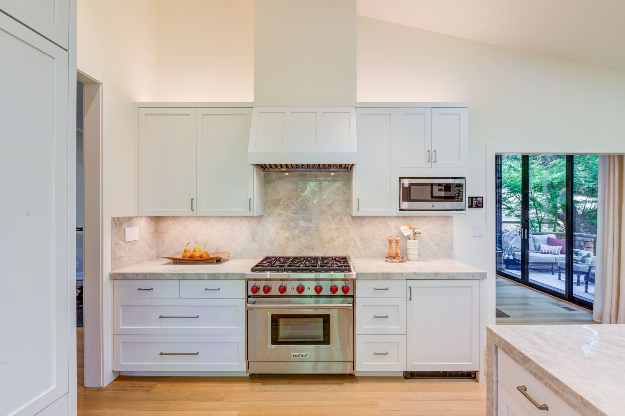 Kitchen cooking wall featuring Levitch fabricated cabinetry, a built-in Wolf range, stone backsplash, and integrated ventilation beneath the vaulted ceiling.