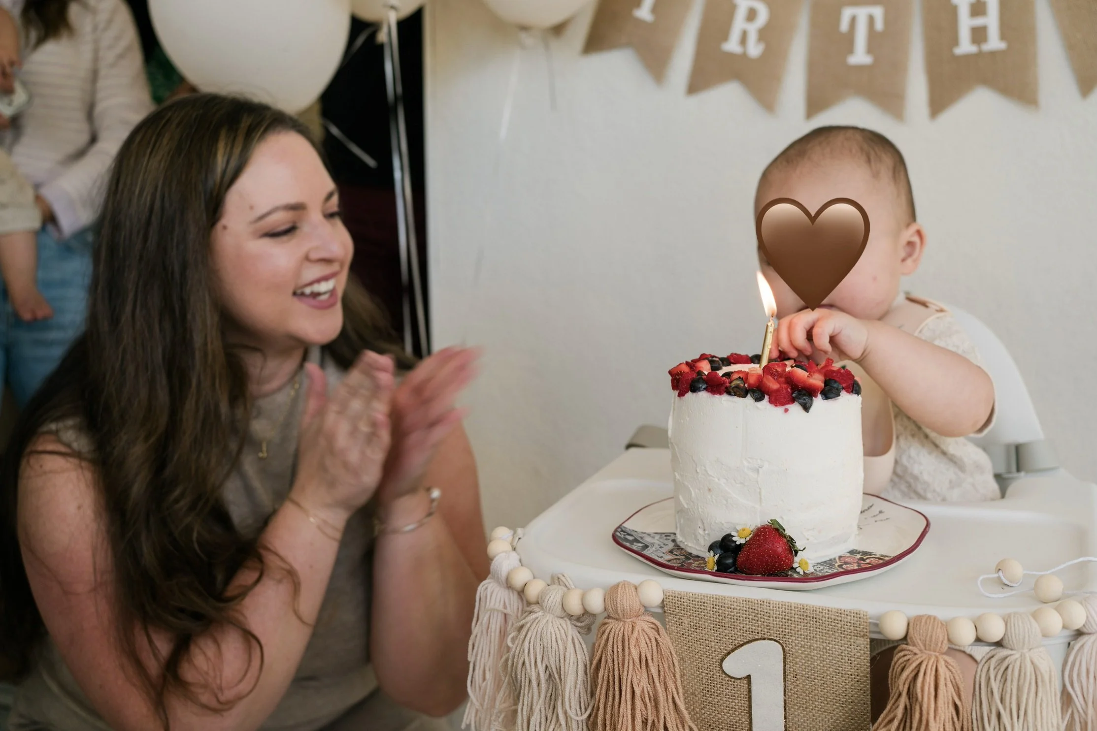Toddler enjoying a berry-topped smash cake during a pancake-themed first birthday celebration with a neutral birthday banner and high chair decorations.