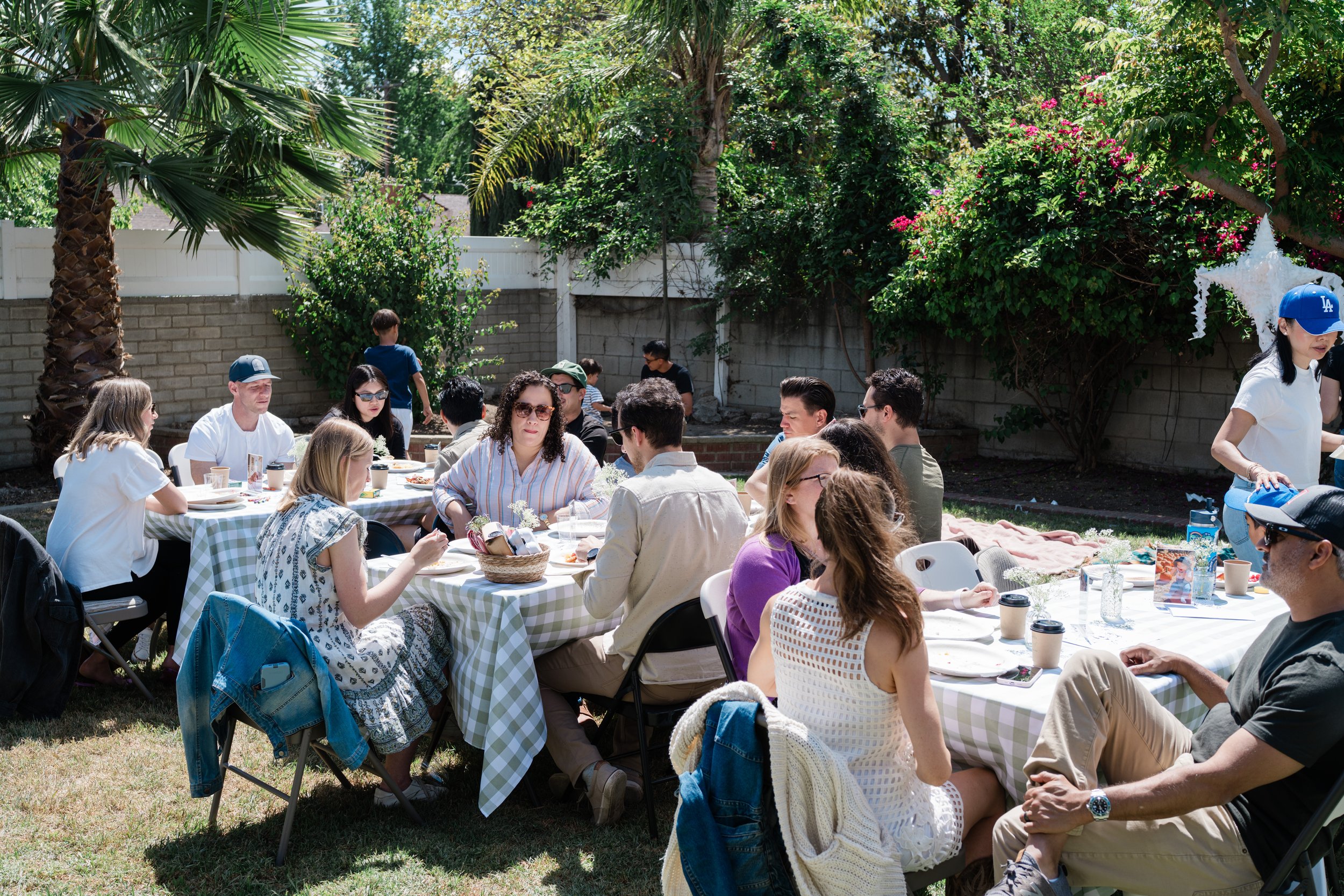 Guests enjoying an outdoor pancake-themed first birthday party with green gingham tables, backyard brunch seating, and family-friendly decorations.