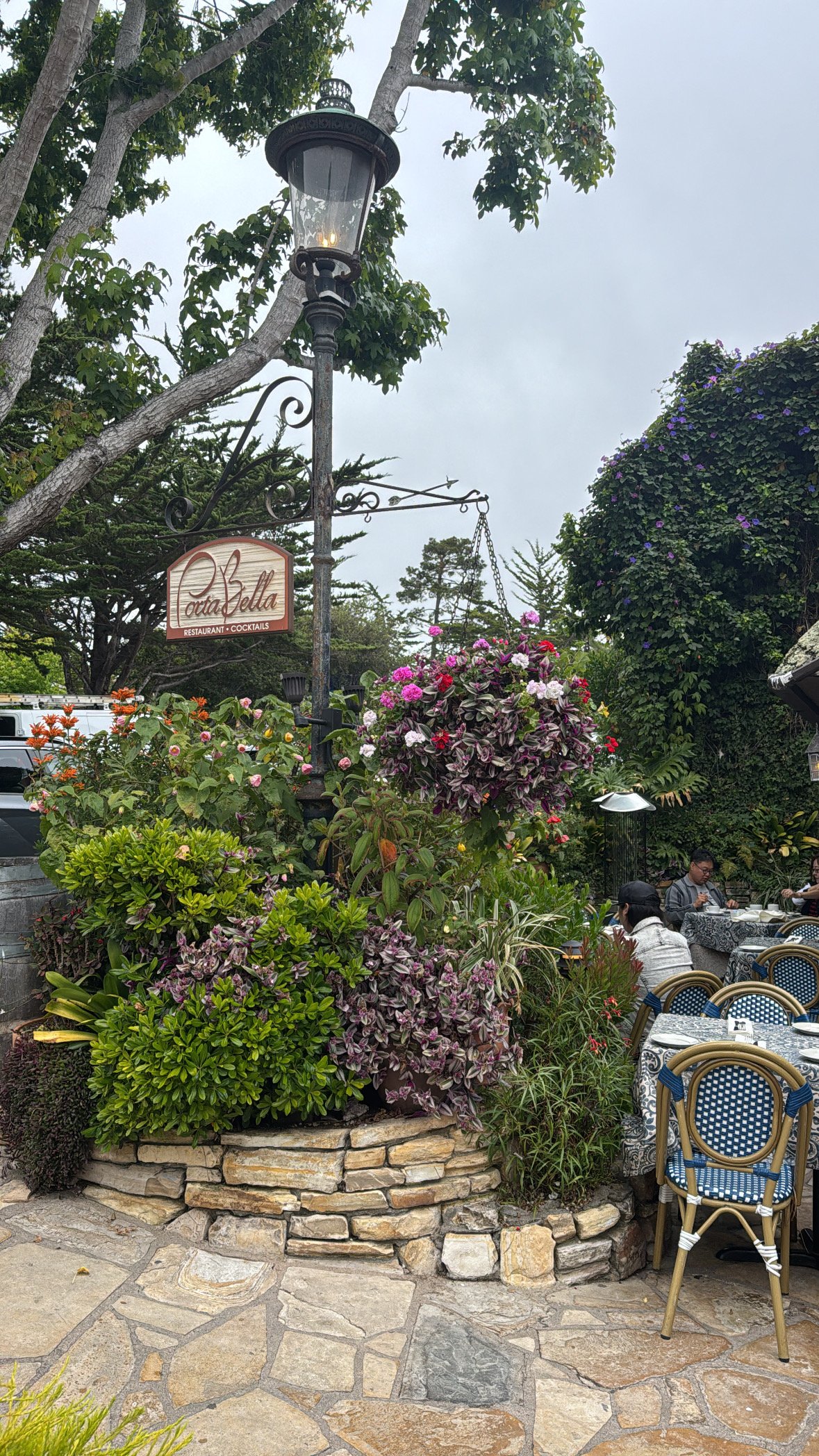 Outdoor dining patio at Porta Bella restaurant in Carmel-by-the-Sea, California, featuring colorful flower gardens, stone pathways, and a cozy atmosphere for a leisurely meal.