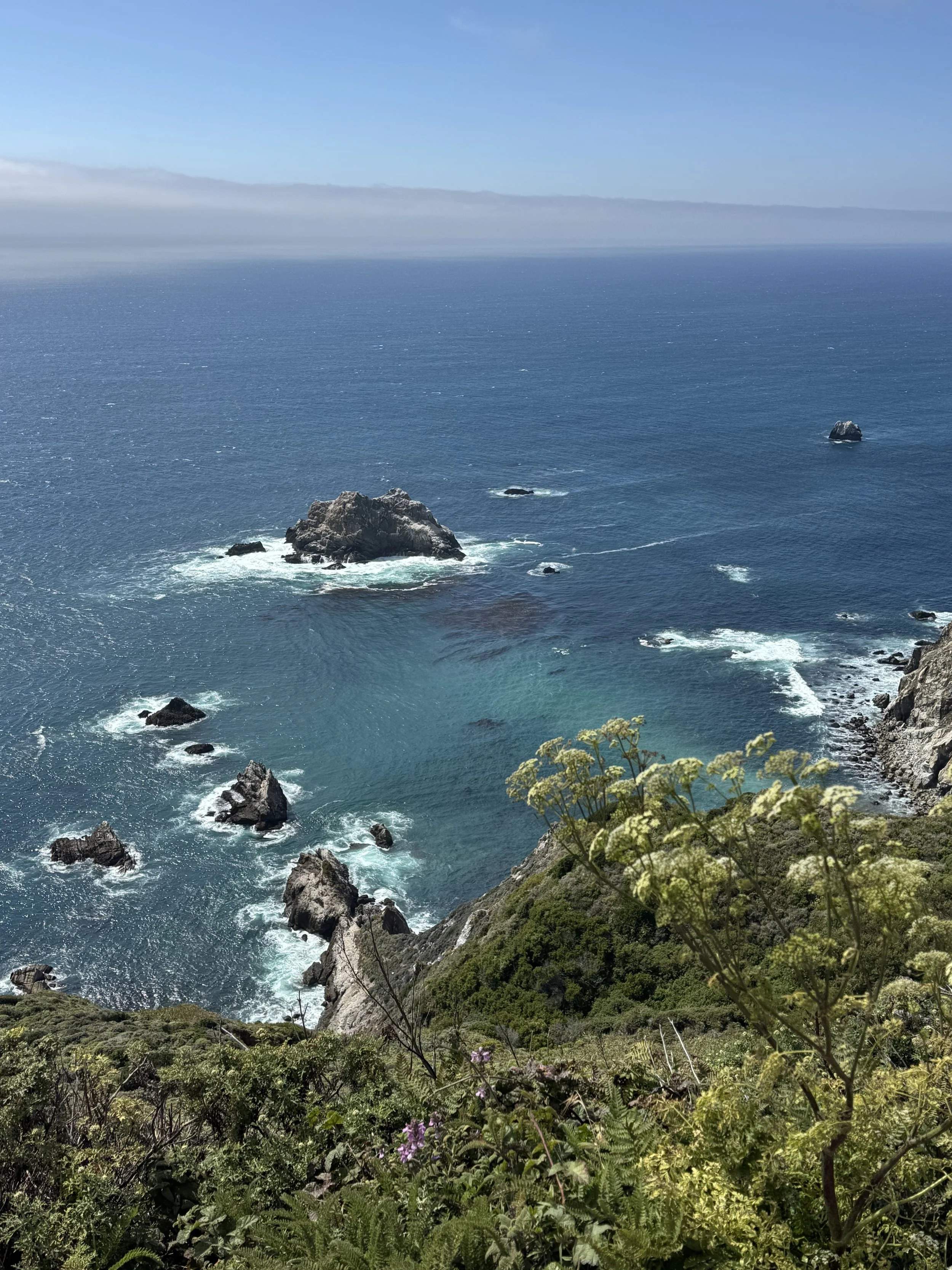 Panoramic view of the Big Sur coastline south of Bixby Bridge, featuring rocky sea stacks, turquoise Pacific Ocean water, and rugged coastal cliffs.