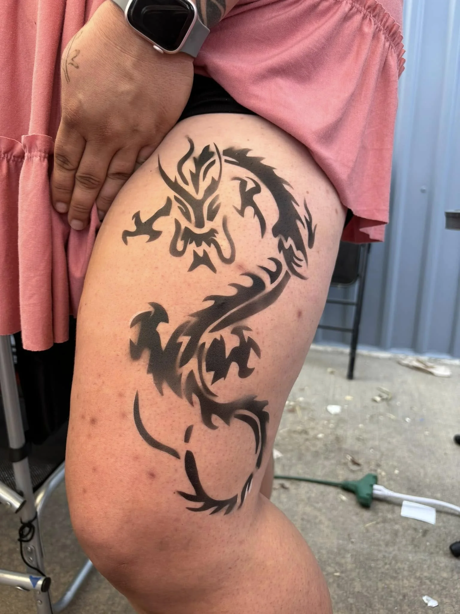 A person's thigh with a large black tribal-style dragon tattoo.