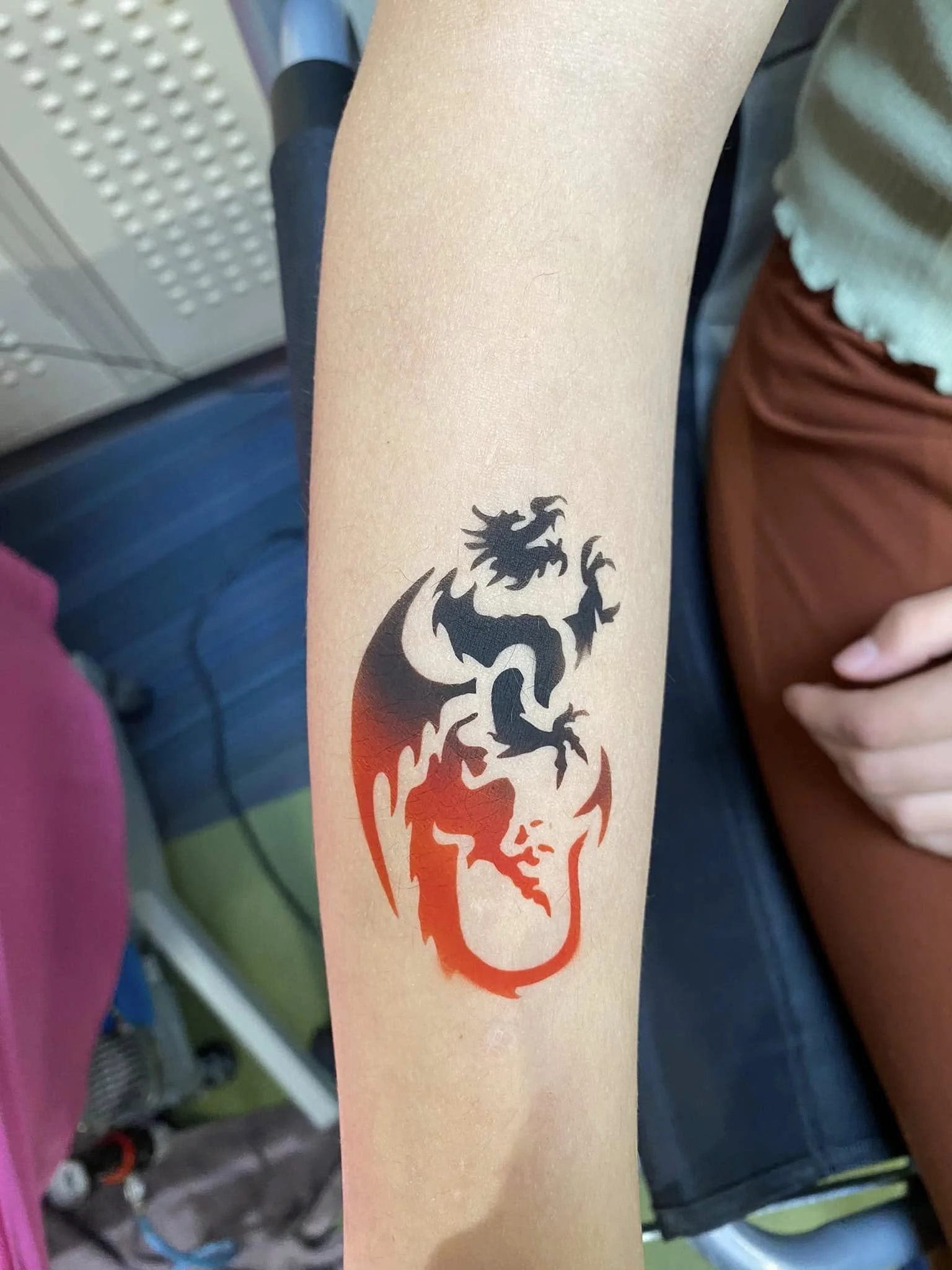Temporary tattoo of a stylized black and red dragon in a vertical stance on a person's forearm.