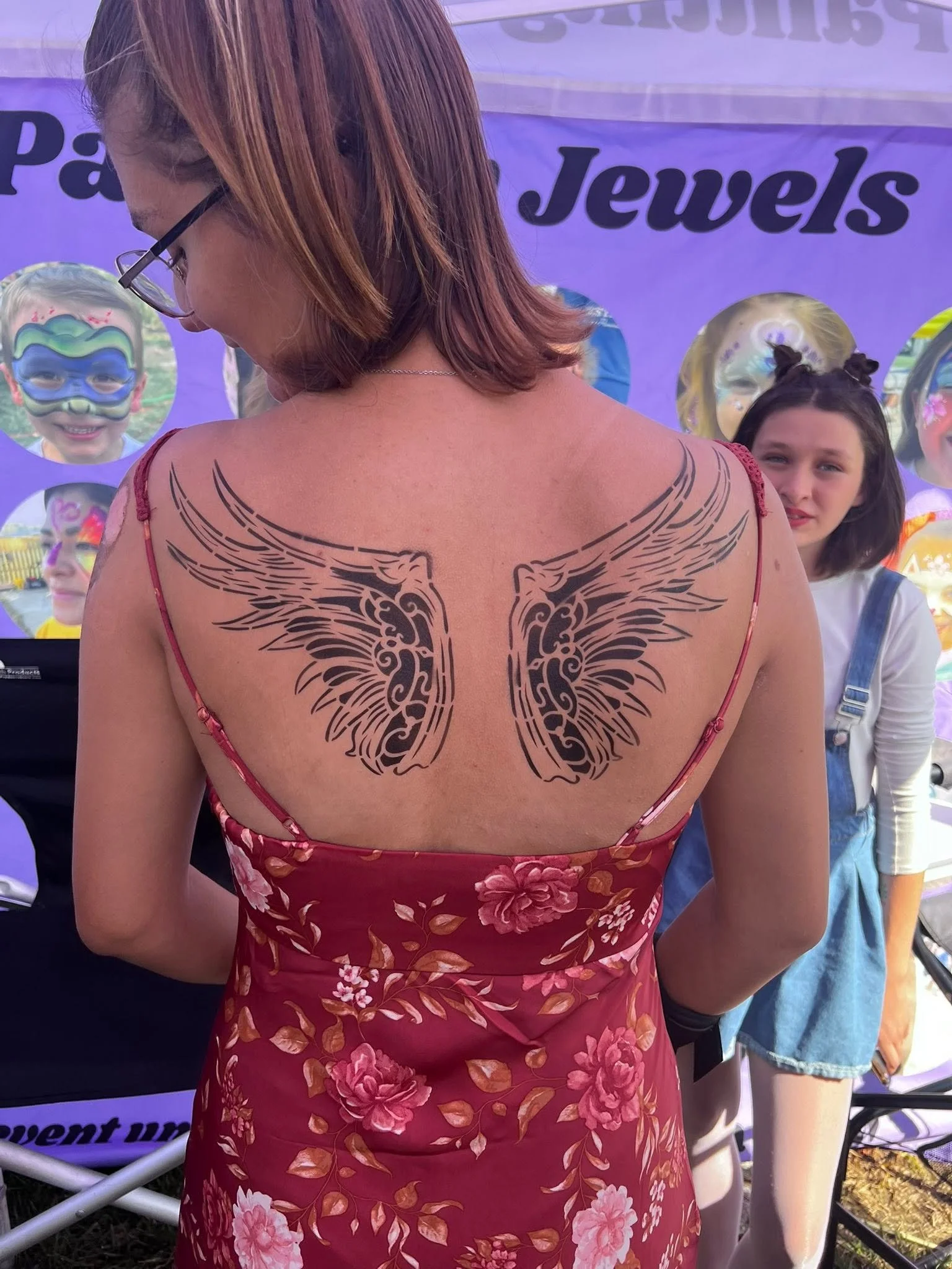 Back of a woman wearing a red floral dress with a angel wings tattoo art. 