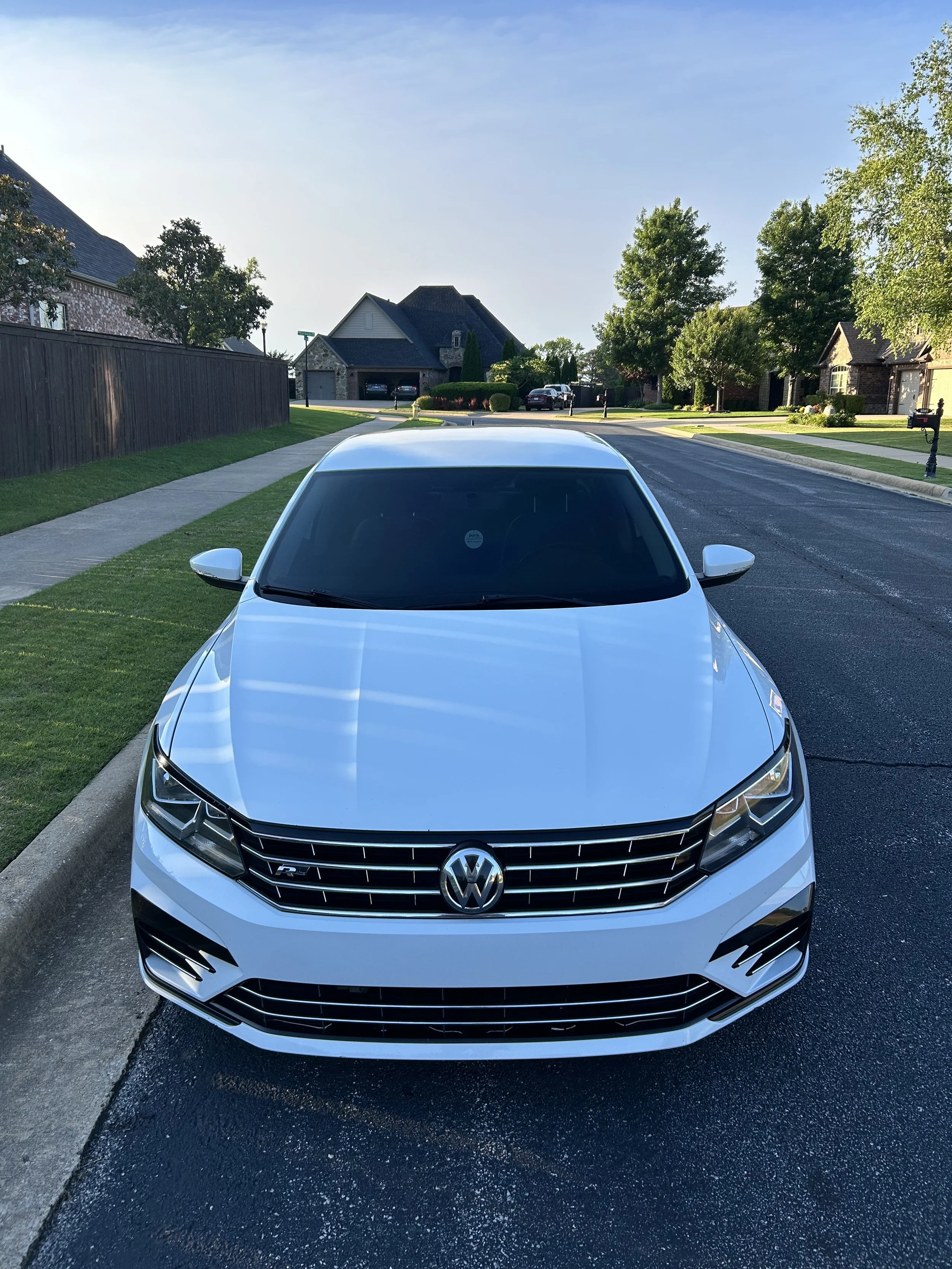 Front view of a white Volkswagen sedan parked on a suburban street in the early morning or late afternoon.