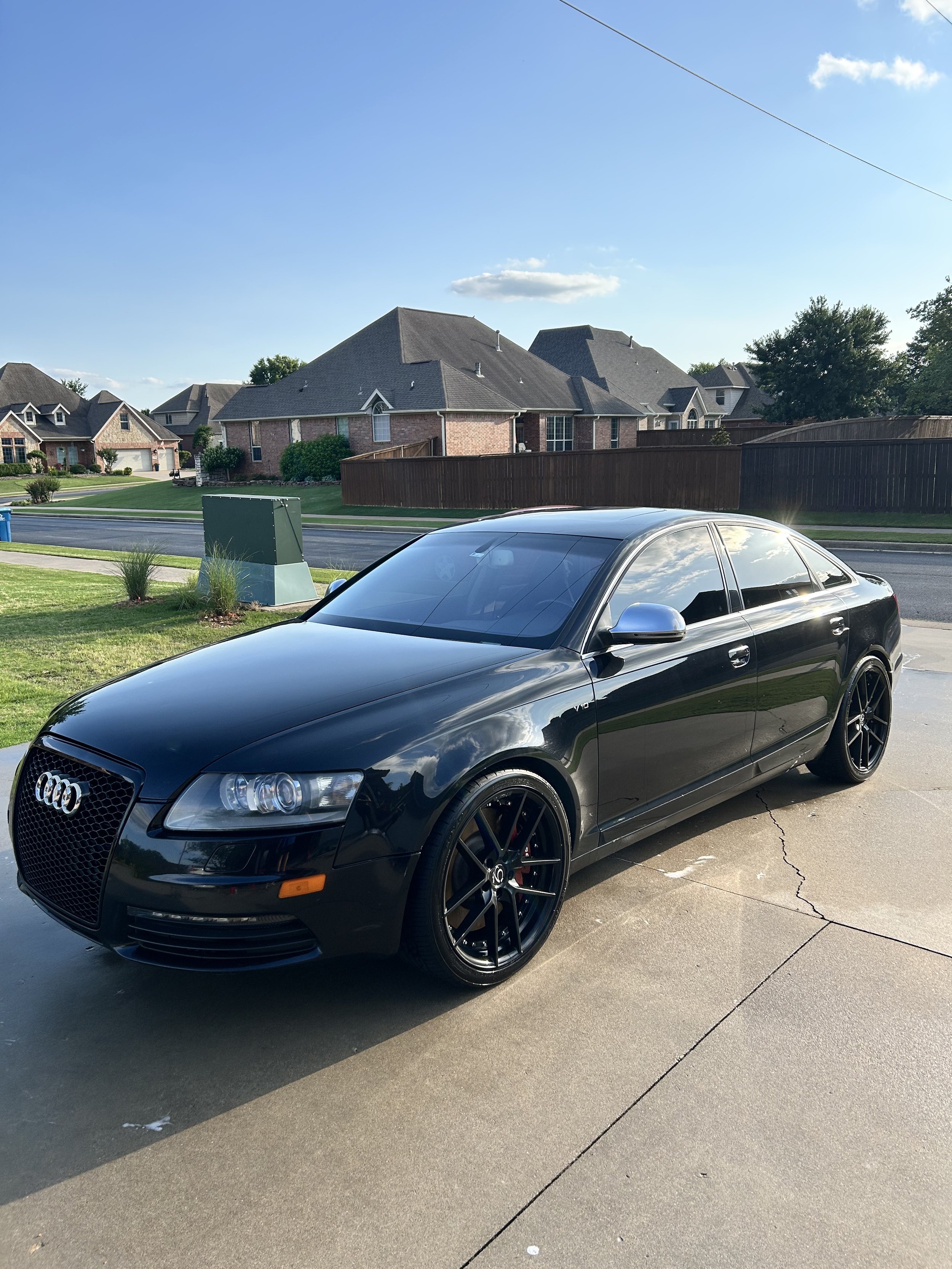 Black Audi sedan parked on a suburban driveway with a clear blue sky and houses in the background.