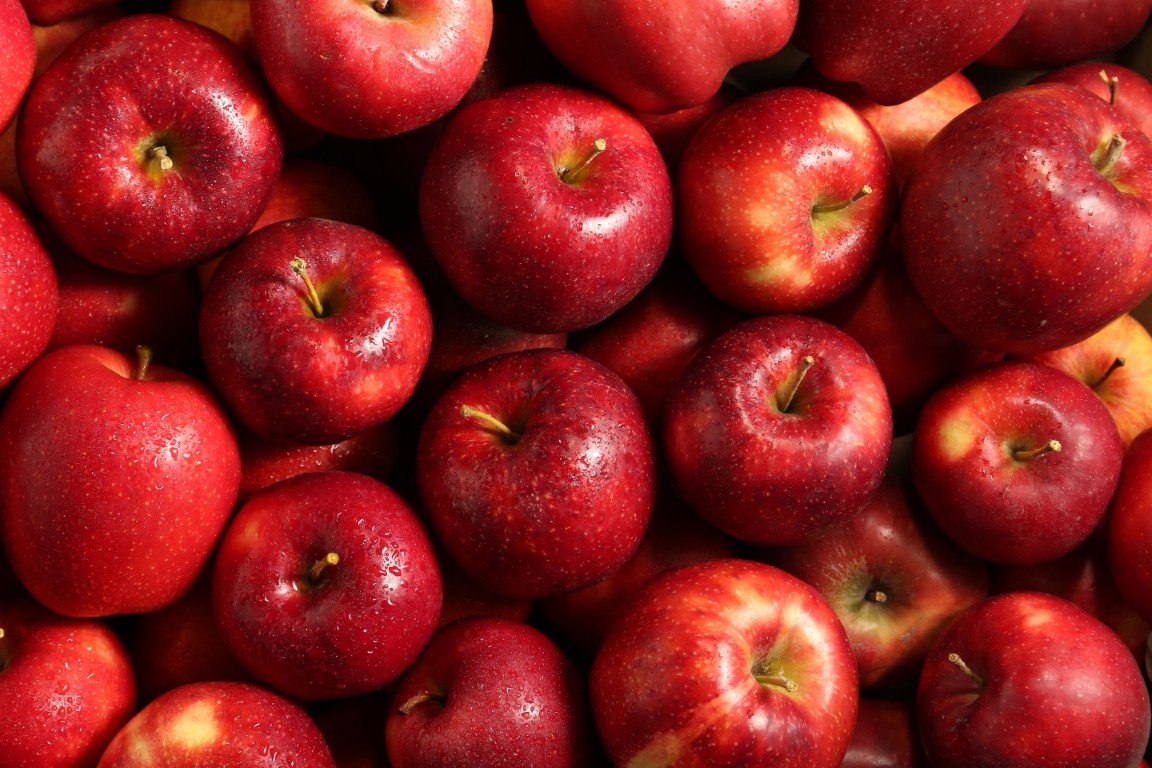 A close-up view of many fresh red apples with some water droplets, piled together.