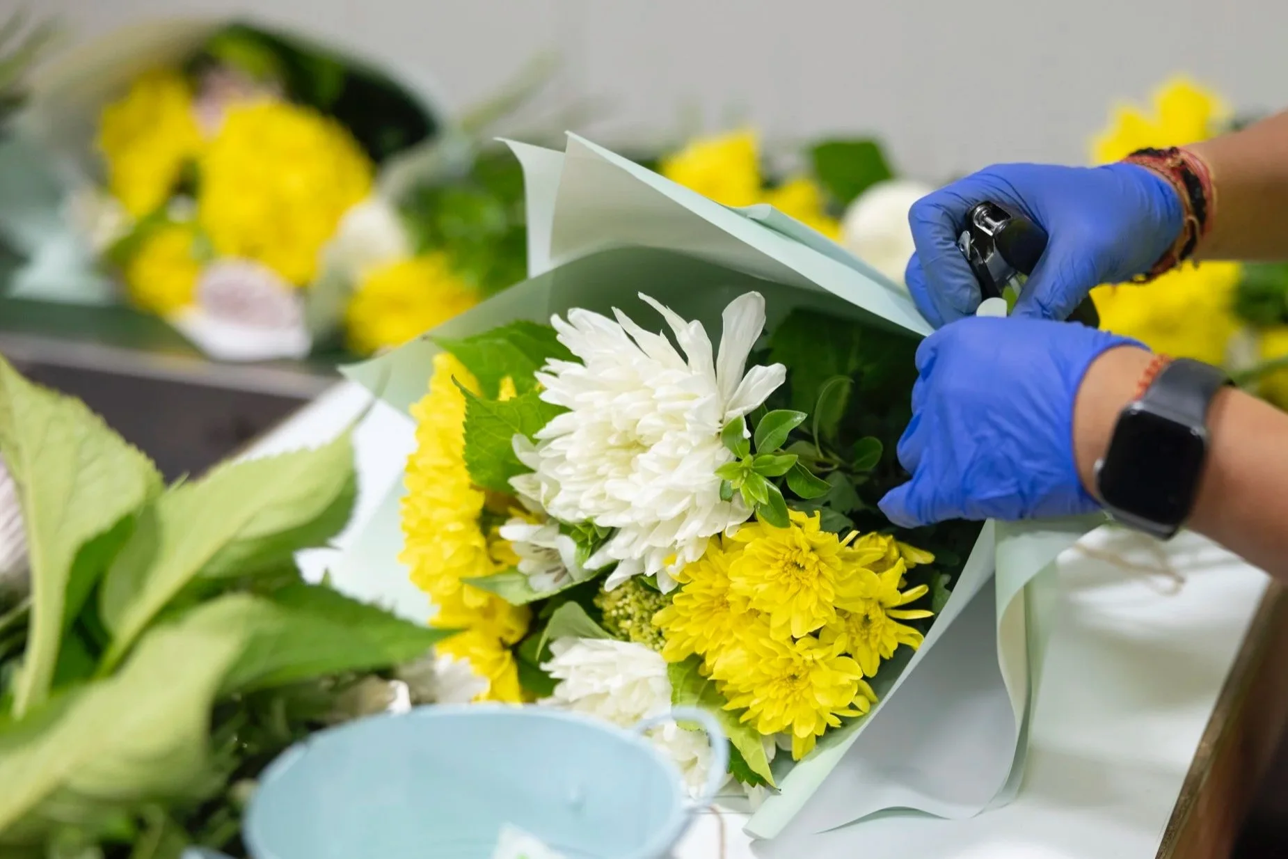 Person arranging a bouquet of white and yellow flowers with blue gloves.