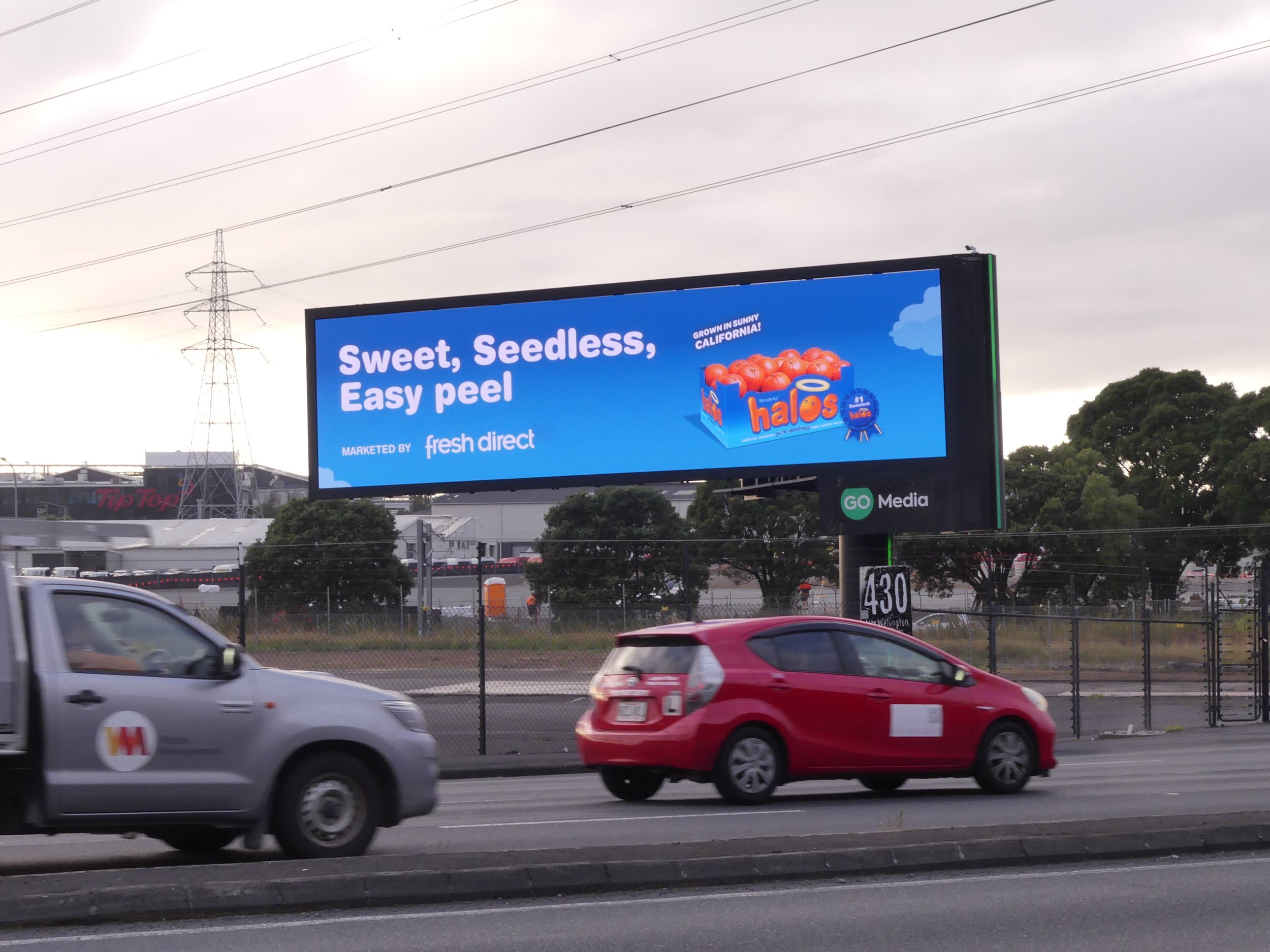 Billboard advertisement for Halo tomatoes, with the slogan 'Sweet, Seedless, Easy peel.' It shows a box of tomatoes and mentions they are grown in Sunny California.