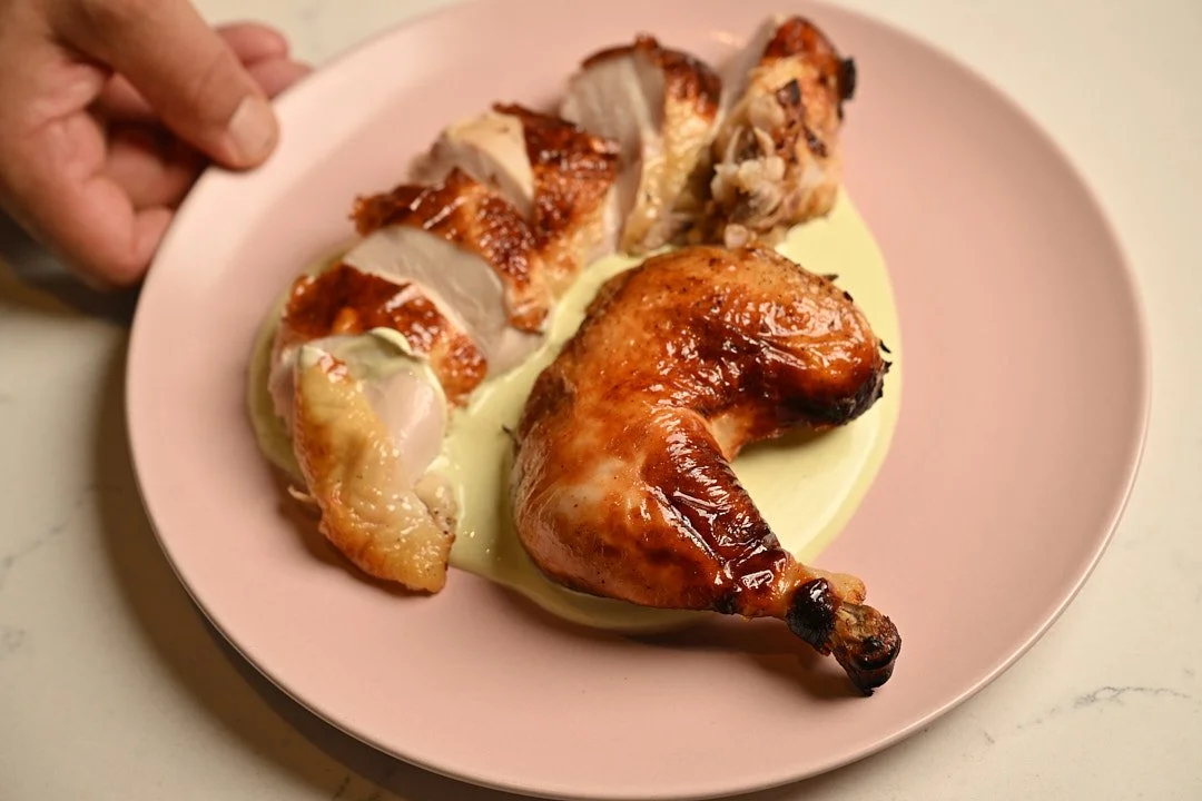Roasted chicken on a bed of green herbed yogurt sauce, on a pink plate being handed to you.