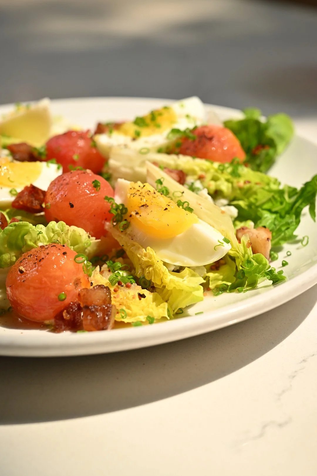 Close up image of crisp lettuce with tomato, egg, blue cheese crumble, bacon.
