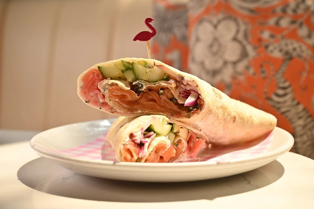 A wrap with salmon and cucumber on a white plate with a pink flamingo pick.