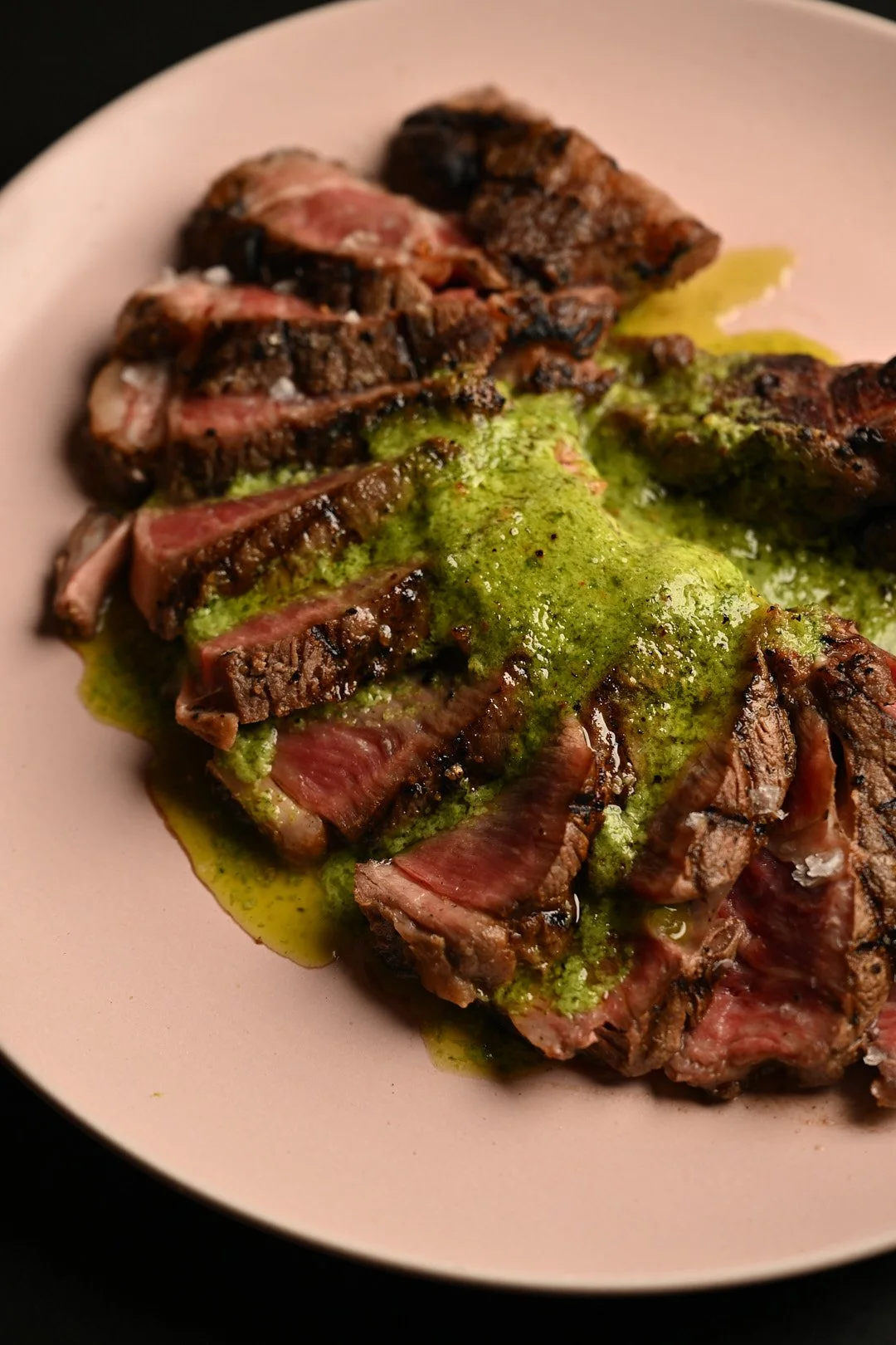 A medium rare steak, sliced and topped with a green chimichurri butter.
