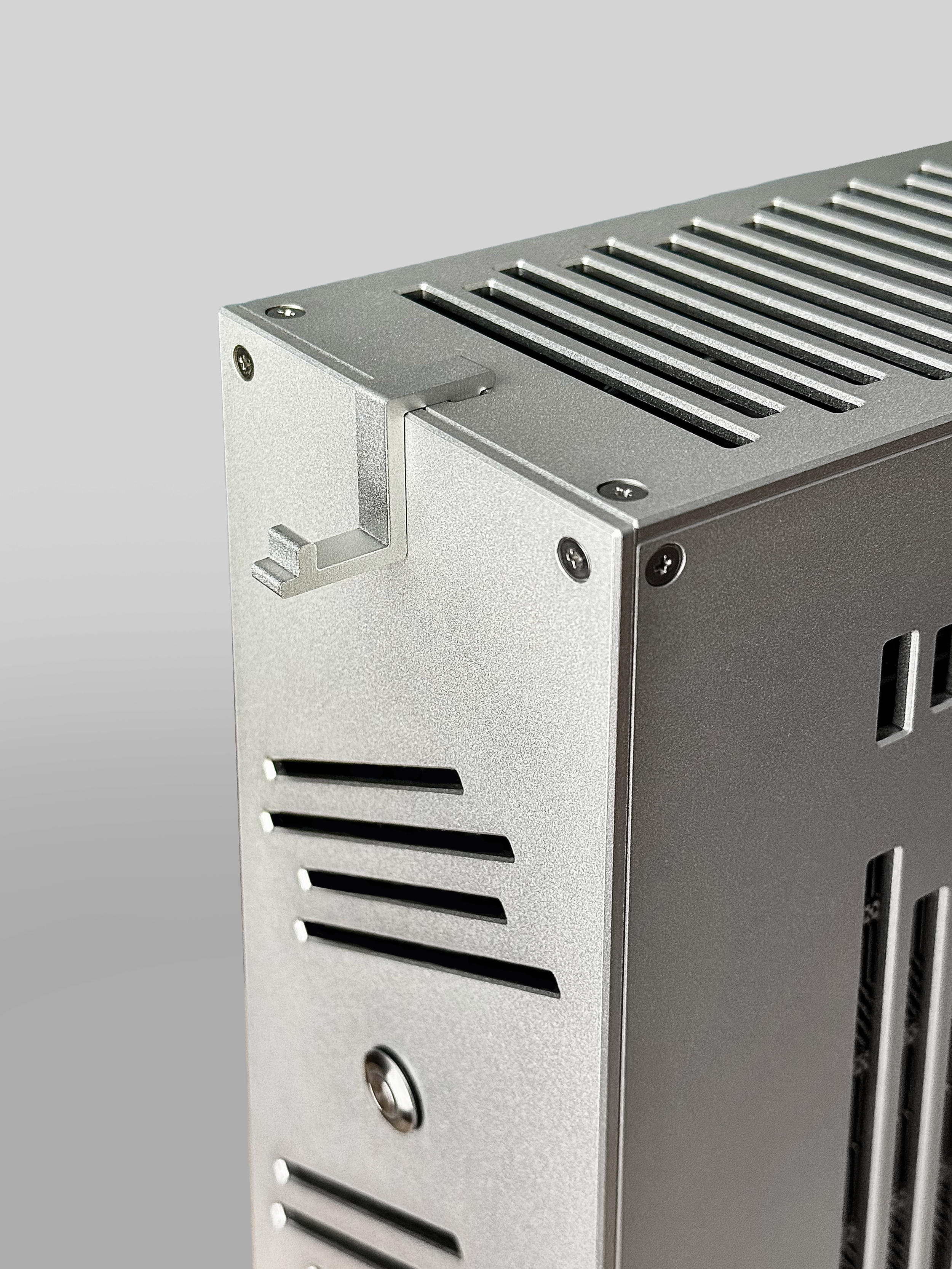 Close-up of a metallic electronic device with ventilation slots and screws on a gray background.