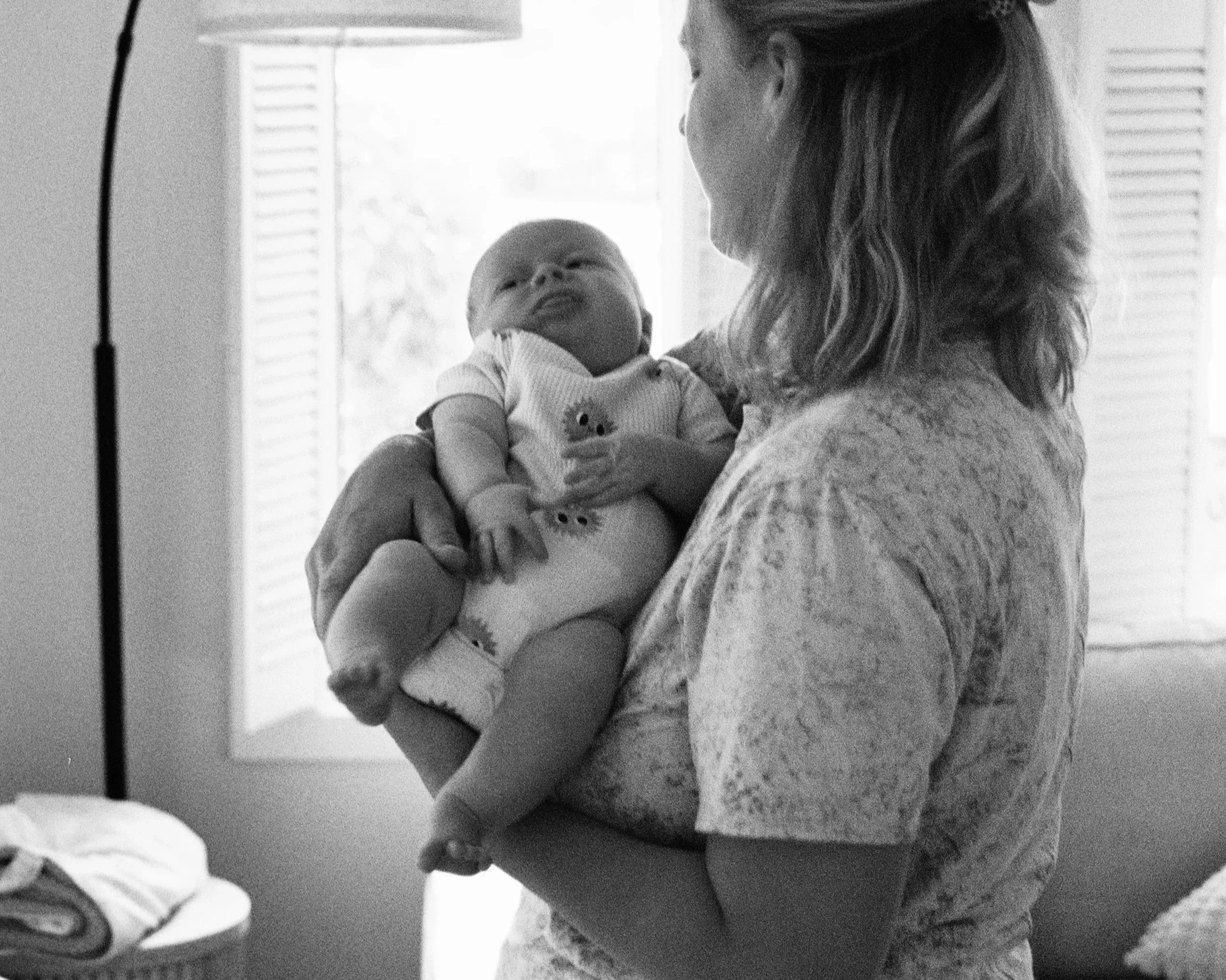 A woman holding a baby in a room with sunlight coming through the window.