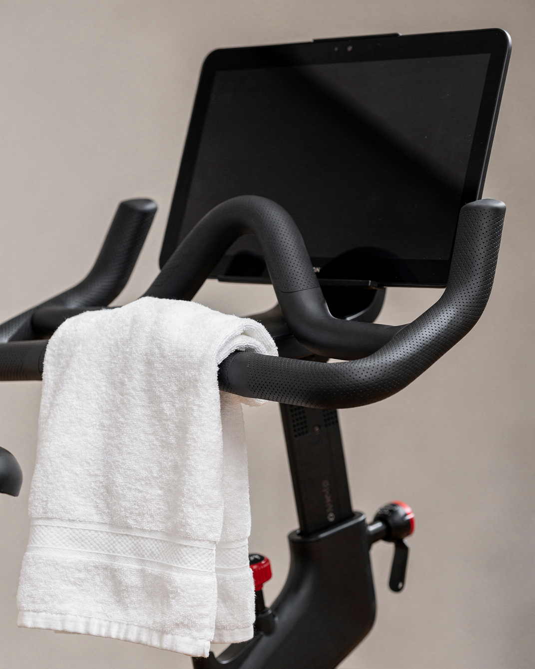 Indoor exercise bike with a white towel draped over the handlebars and a mounted screen display.