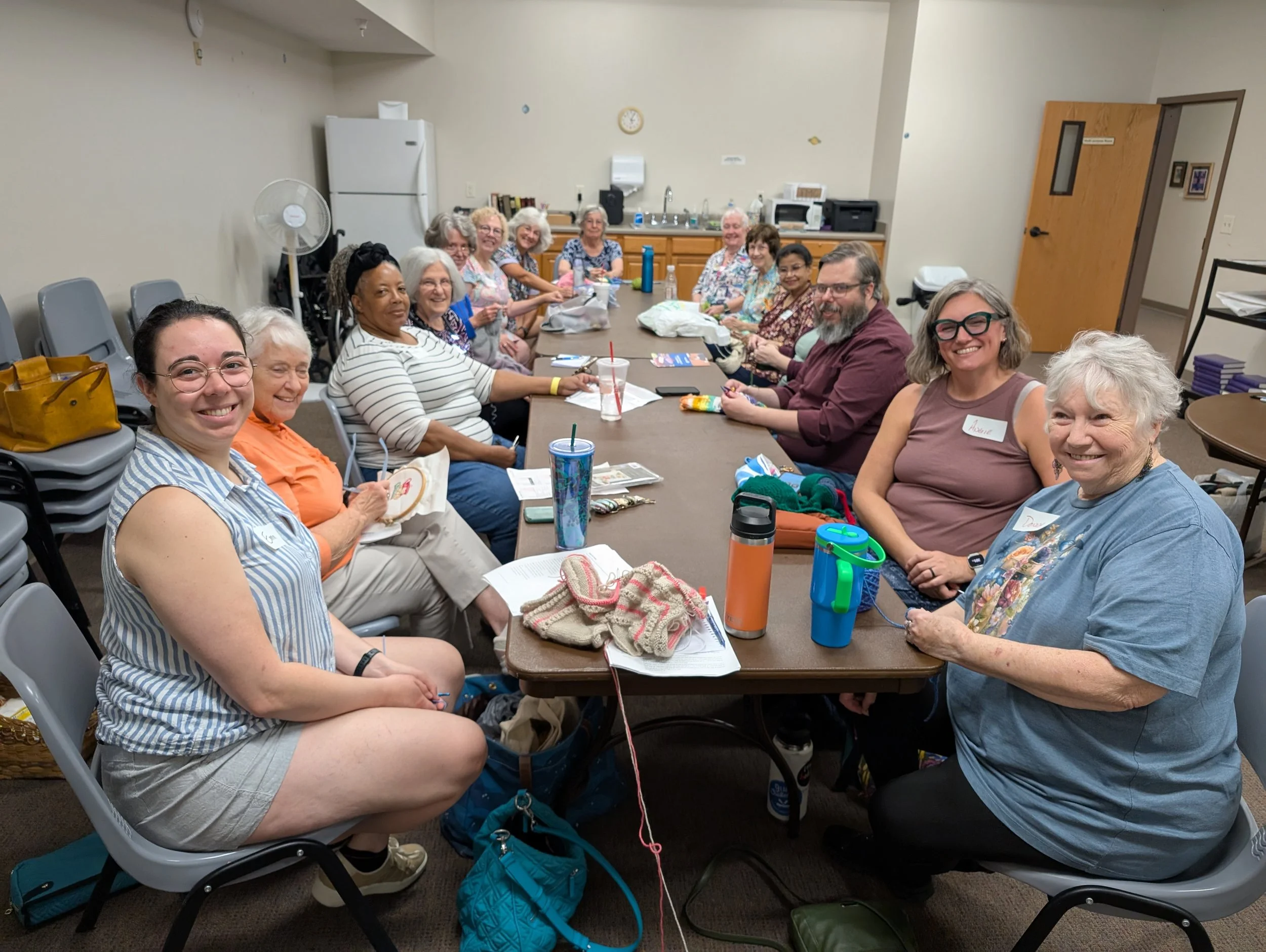 A group of women and a man sitting around a long meeting table in a room, smiling for the camera.