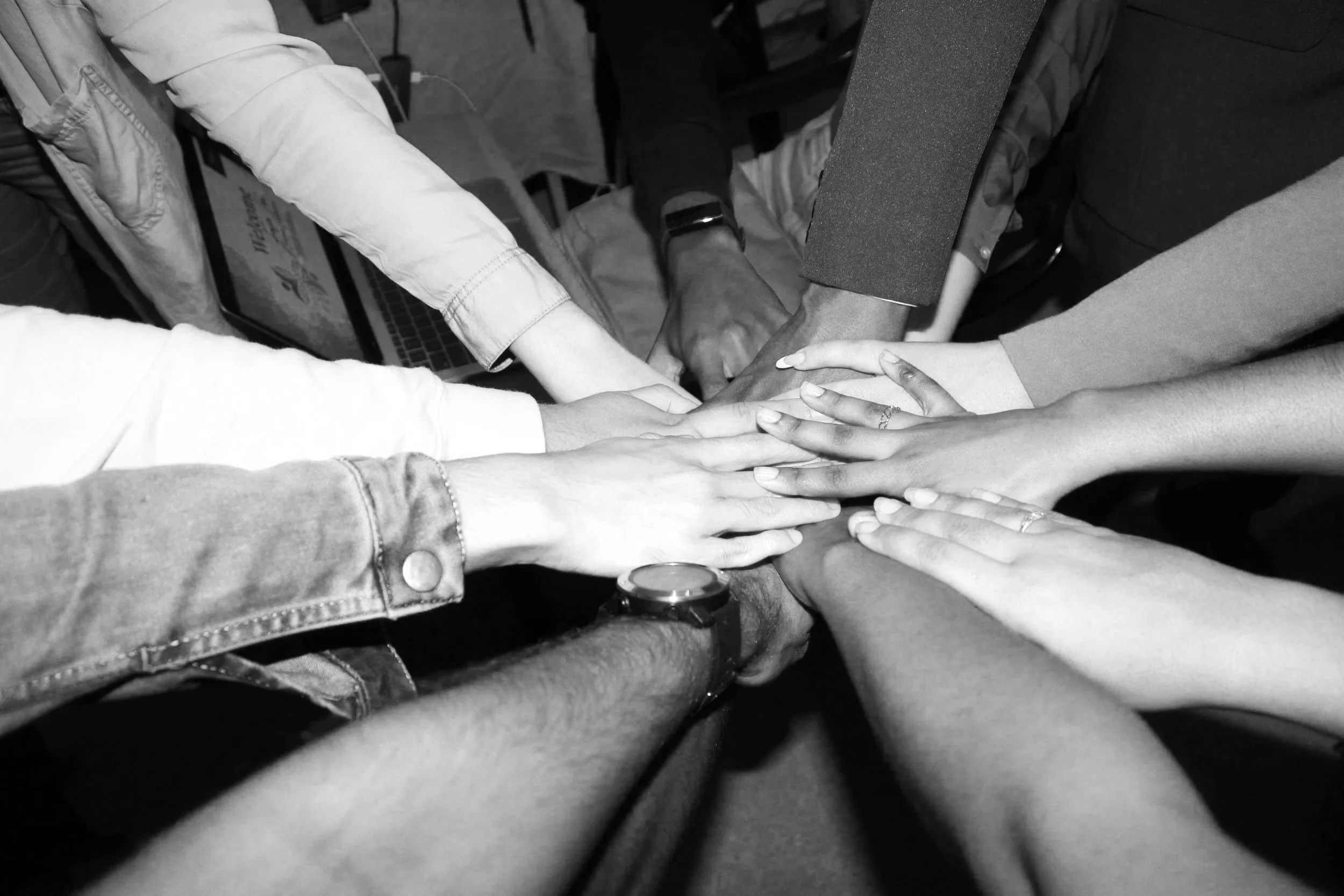Multiple hands of diverse people stacked together in a display of unity and teamwork, in black and white.