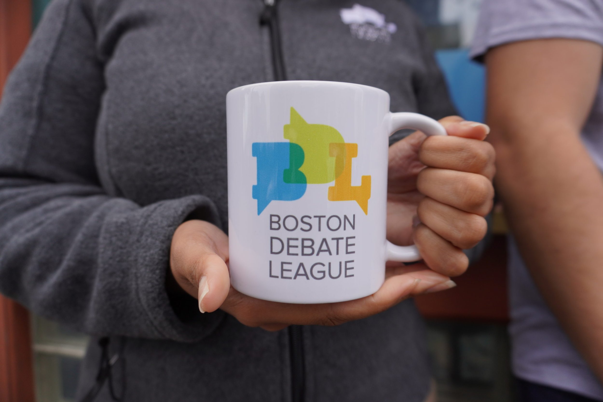 Portrait of a young woman with curly hair, wearing glasses, earrings, and a striped shirt, smiling indoors.