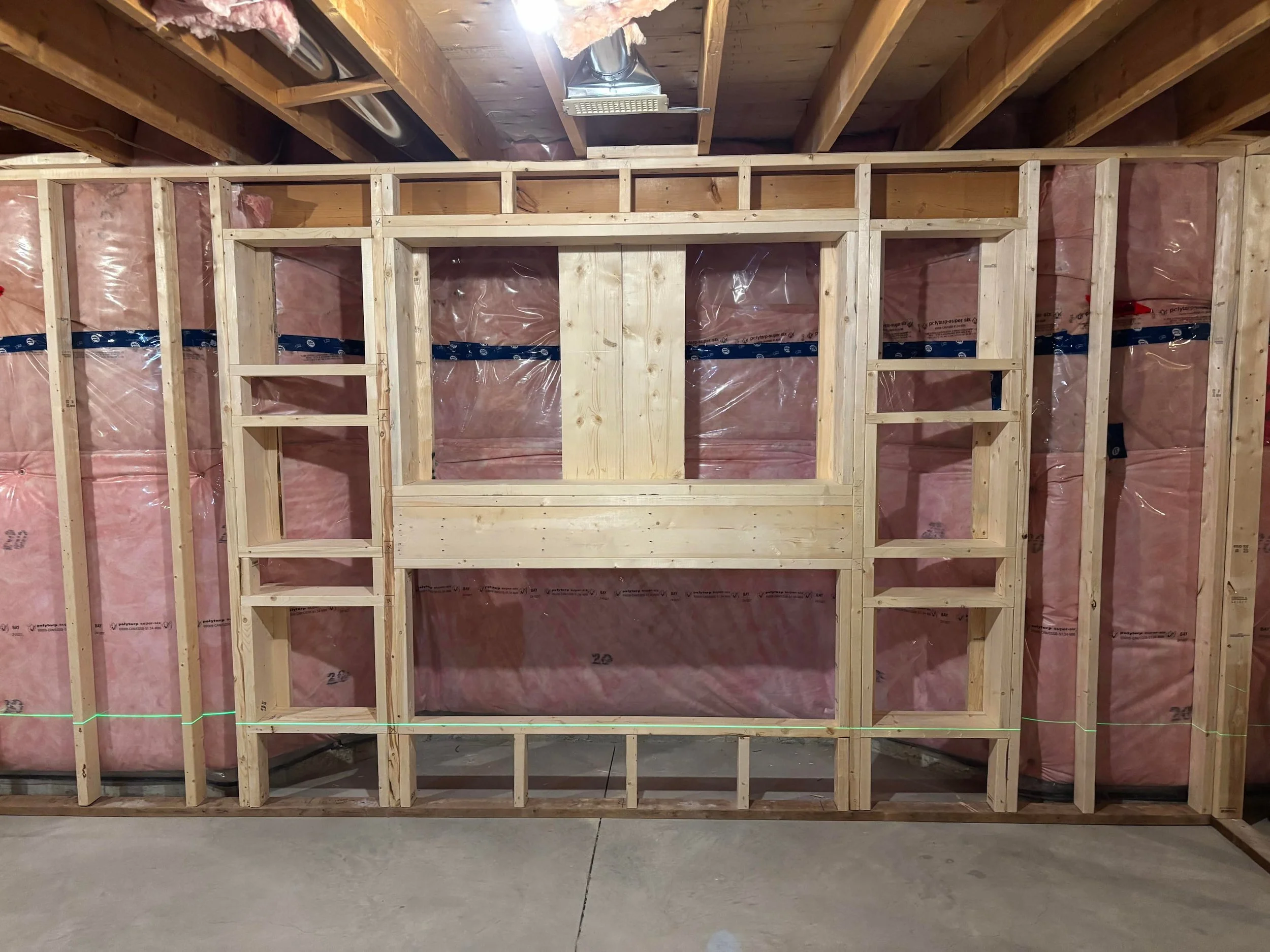 Interior view of a partially built wall framing with pink insulation installed in the wall cavities.