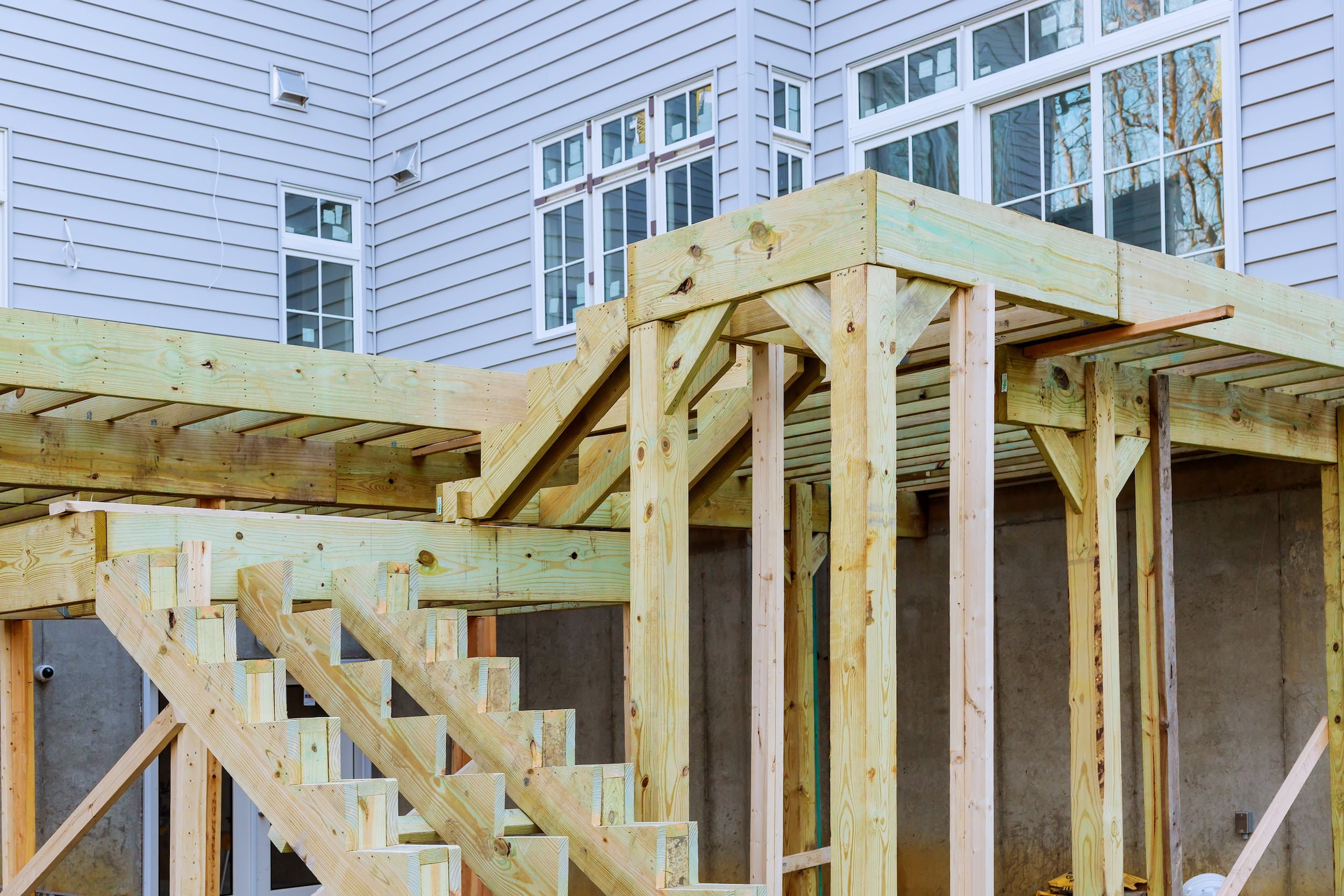 Construction site with a wooden staircase frame under development outside a beige building with large windows.