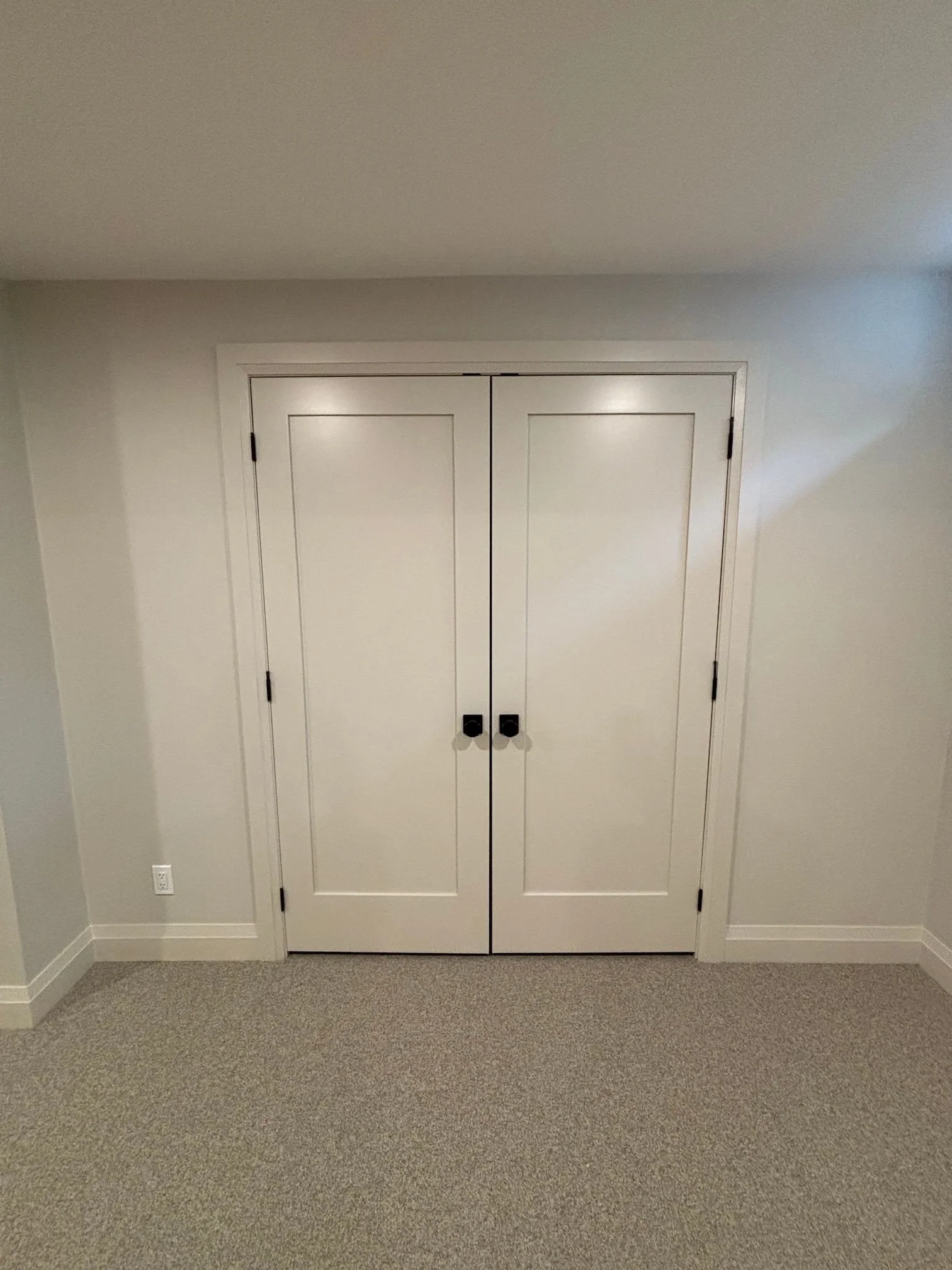 double white closet doors in a beige room with gray carpet and white electrical outlet on left wall