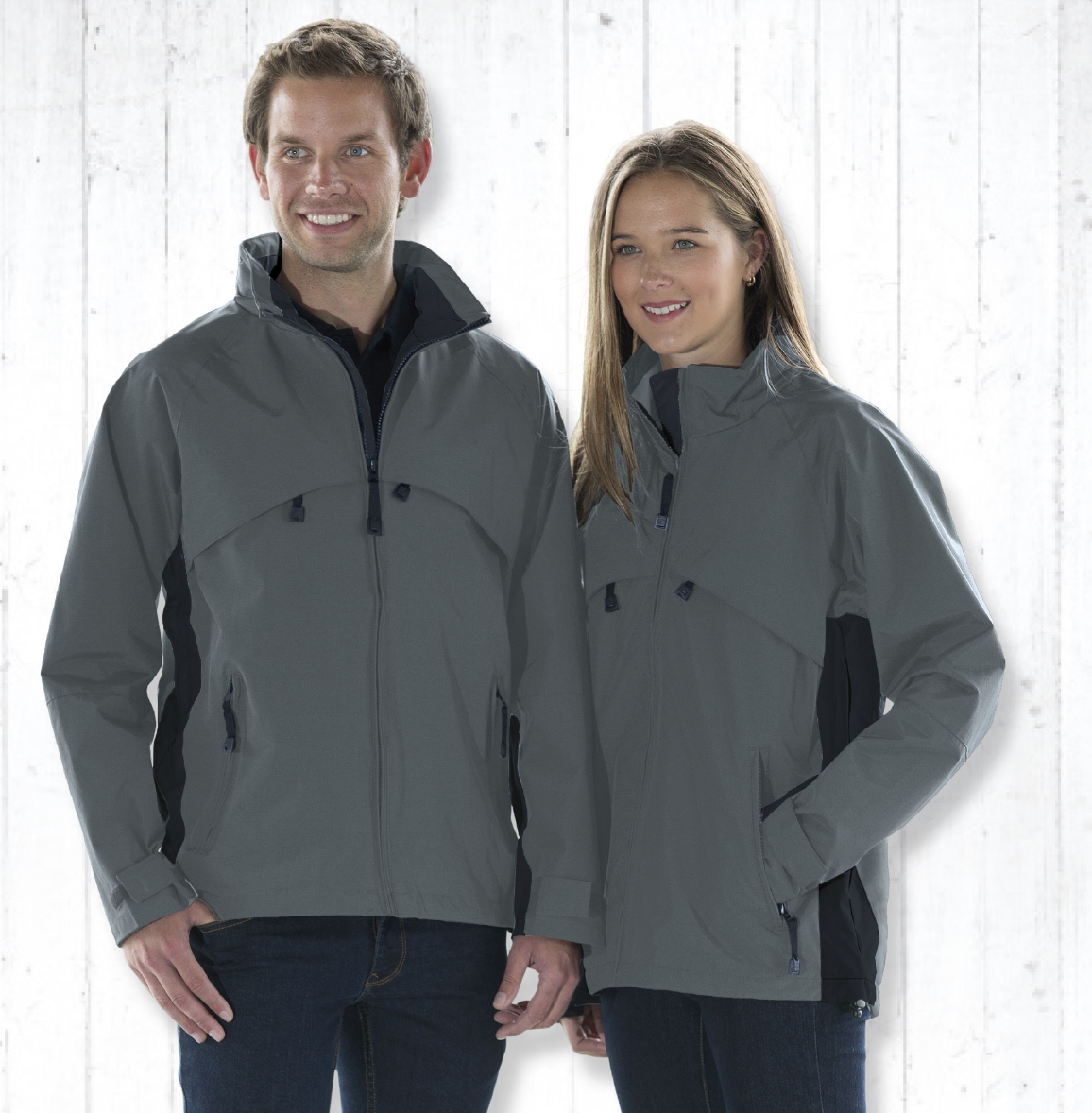 Two young adults, a man and a woman, stand side by side against a light-colored wall. They are wearing black polo shirts with yellow accents on the sides. The man has short, dark hair and is smiling, while the woman has long, light brown hair and is looking off to the side with a neutral expression.