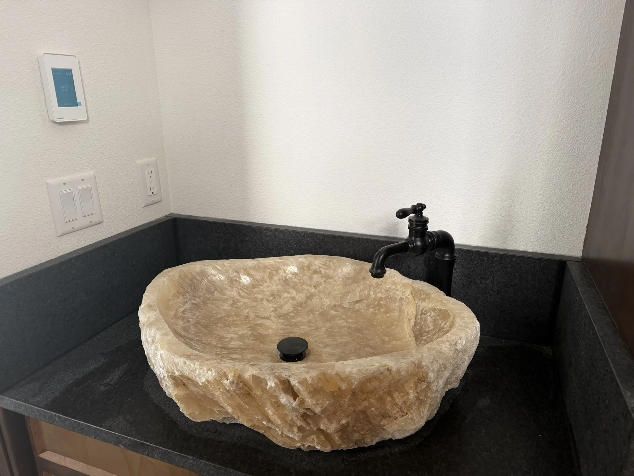 Close-up of a beige marble countertop with a built-in sink and a black faucet in a kitchen or bathroom.