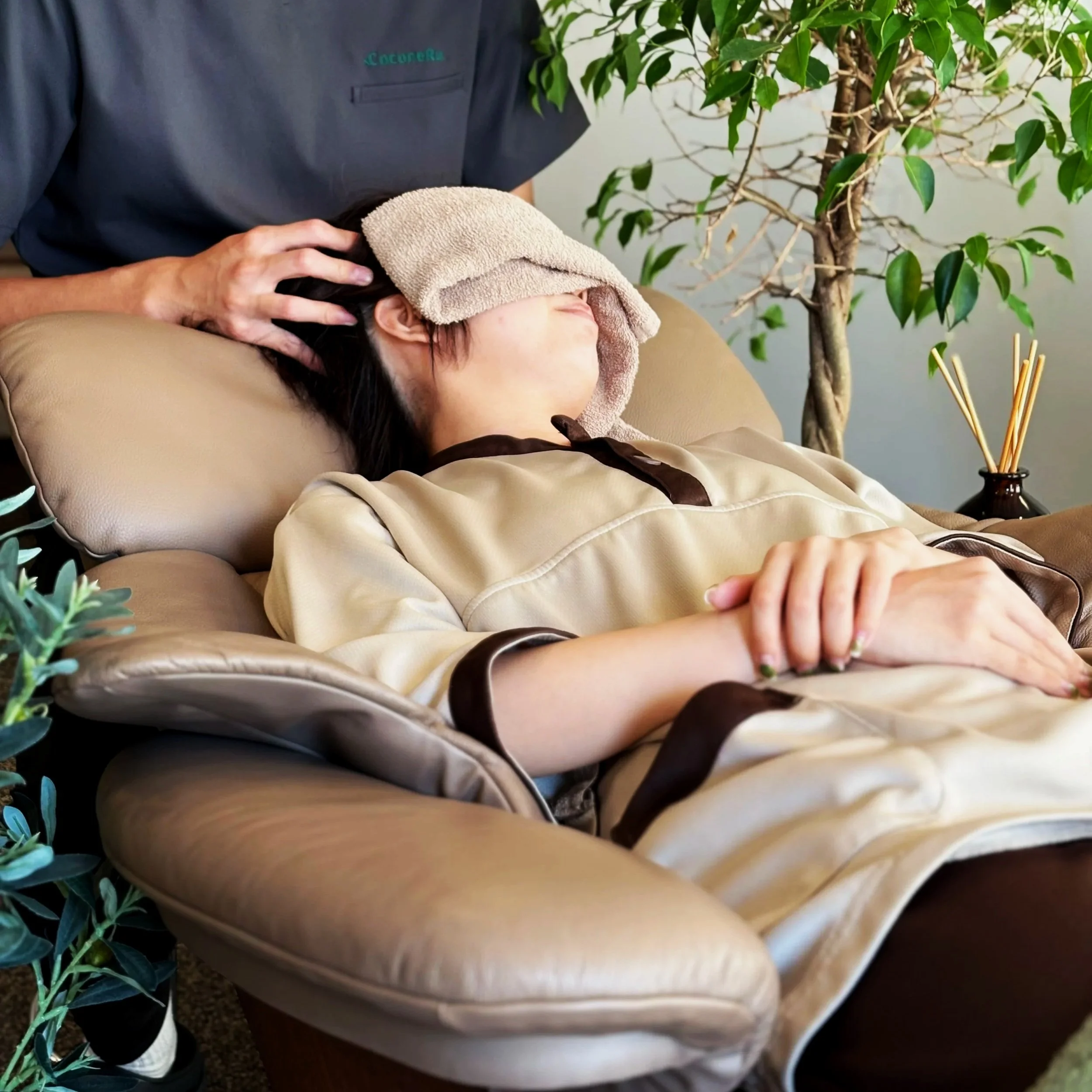 リラックスしている女性にマッサージをしている様子。女性は目隠しをしていて、ベージュのガウンを着ている。