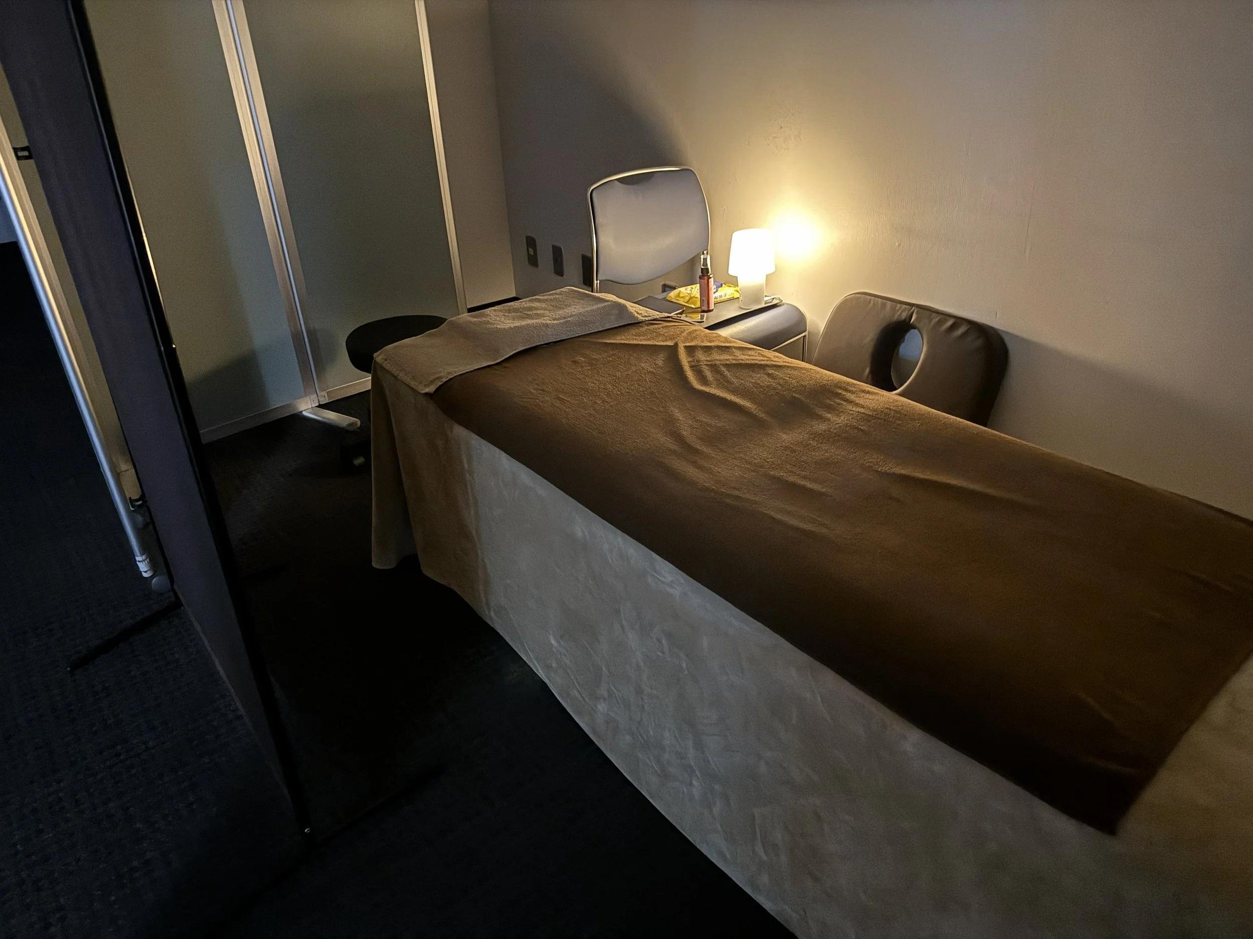 暗い部屋にベッドと小さなテーブル、ランプと椅子が置かれている