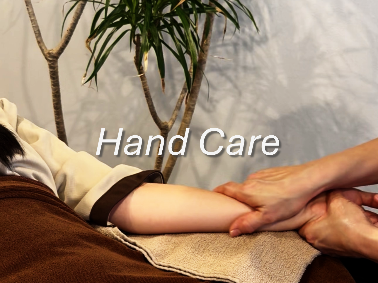 マッサージ師が手を使って手をケアしている様子。背後には植物が置かれている。
