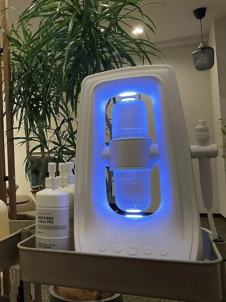 紫色のライトが点灯している酸素濃縮器と消毒液のボトル。室内の植物や照明も見える背景。