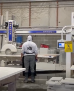 A worker in a factory or warehouse operating a large industrial machine surrounded by boxes and equipment.