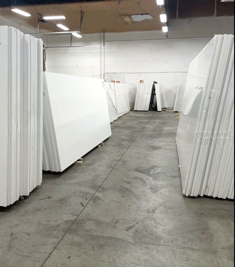 Warehouse aisle with large white panels or boards stacked on pallets.