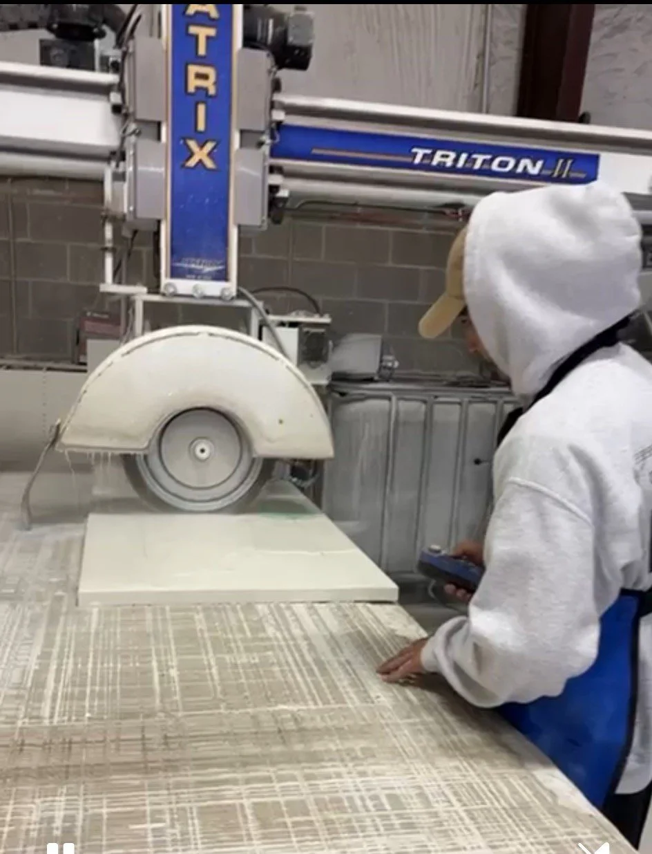 Person in hoodie and baseball cap operating a large industrial saw machine in a workshop.