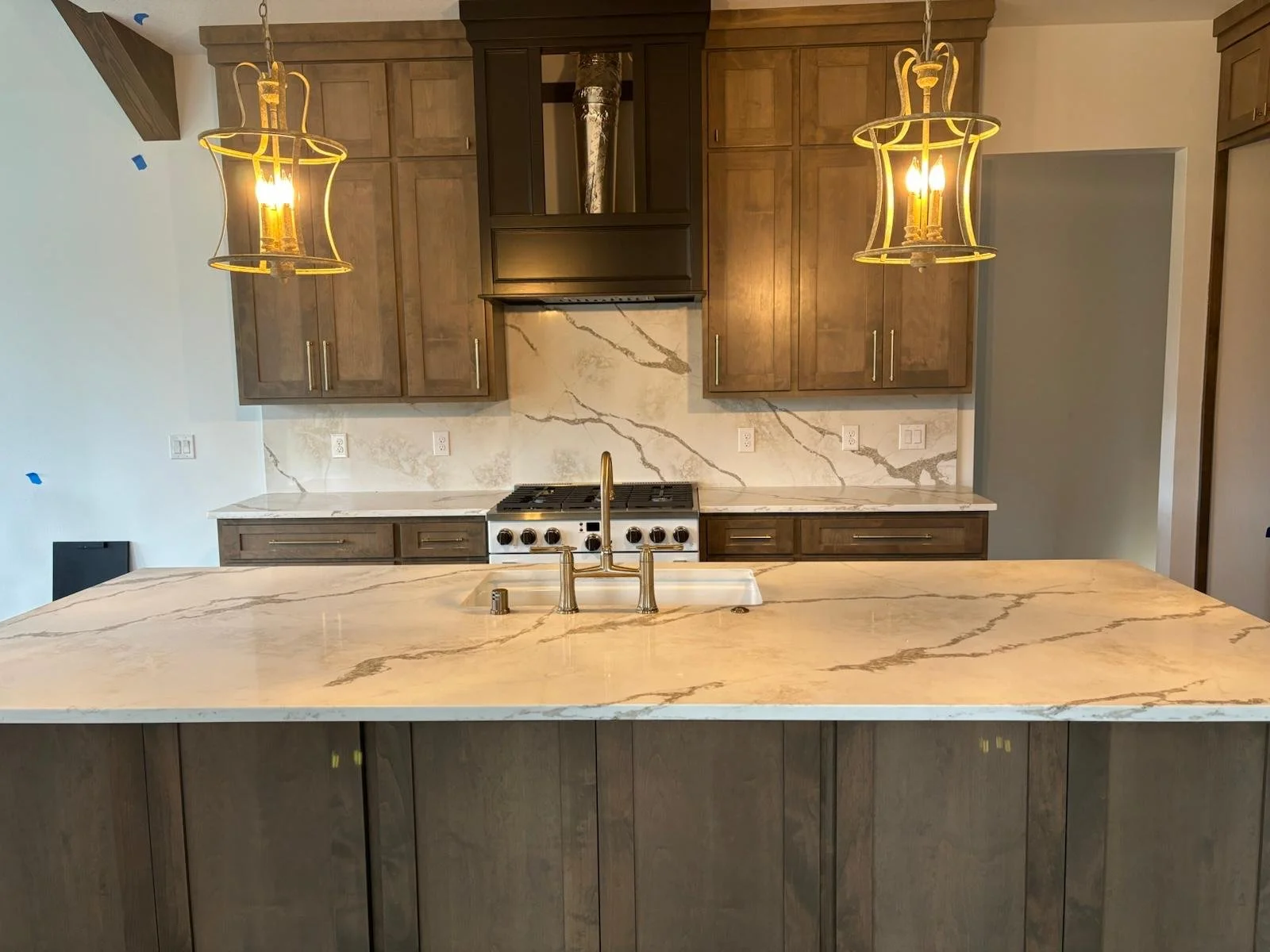 Modern kitchen with wooden cabinets, marble backsplash, marble countertop island, and two pendant lights with gold accents.