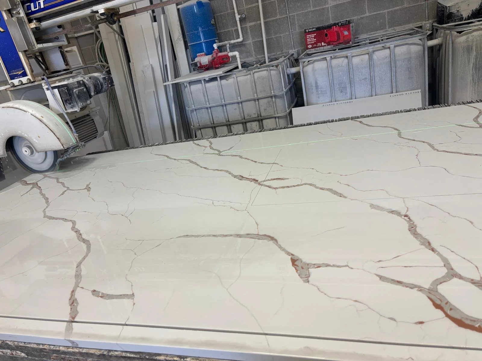 A marble slab with brown and beige veins, situated in a workshop or manufacturing area with tools and equipment in the background.