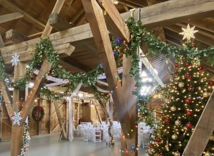 A decorated Christmas party space with a Christmas tree adorned with gold and red ornaments, festive garlands, Christmas lights, and wreaths on the walls. 