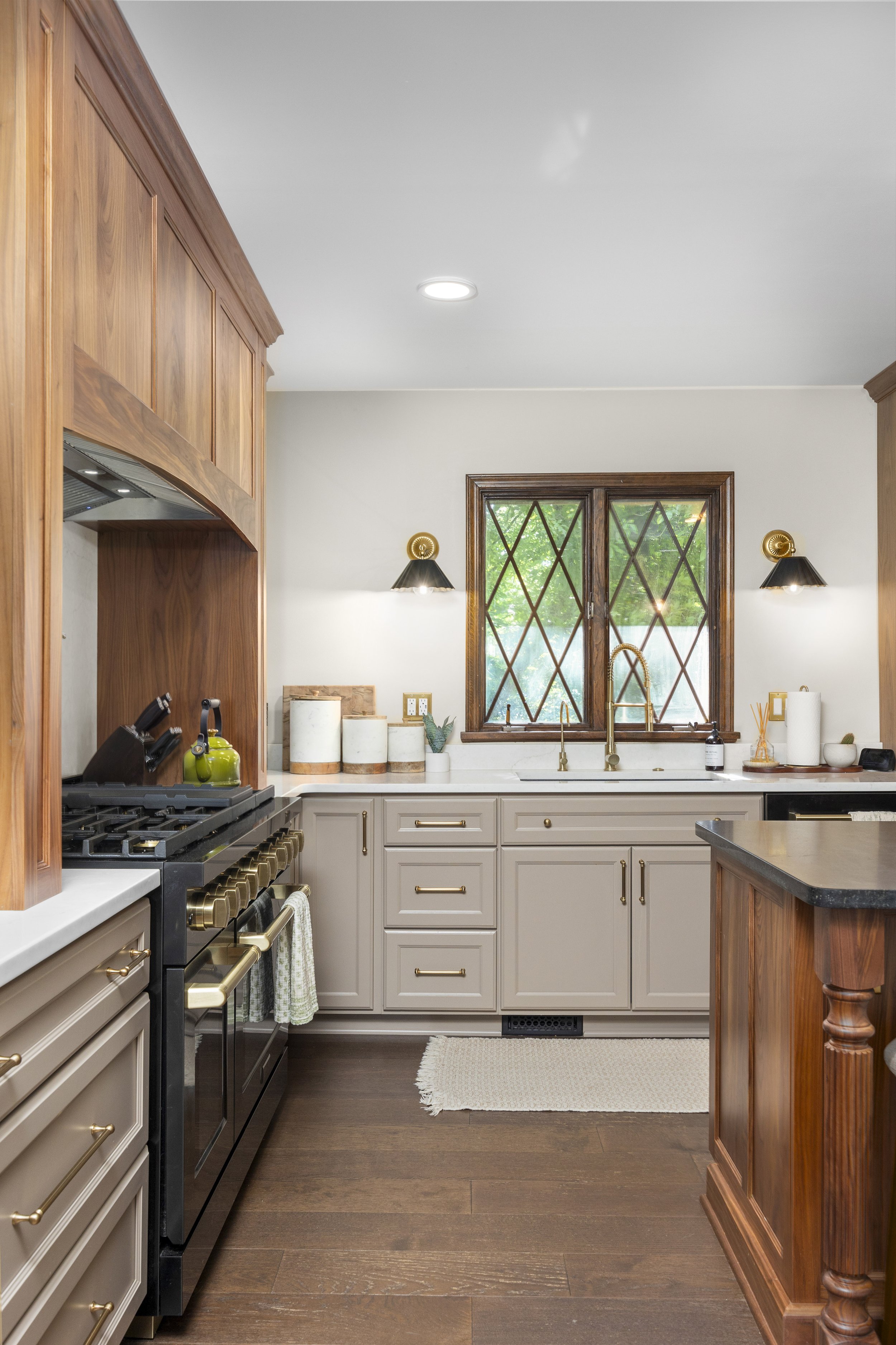 Kitchen with beige cabinets, black stove, granite countertops, window with diamond grid, and decorative wall sconces.