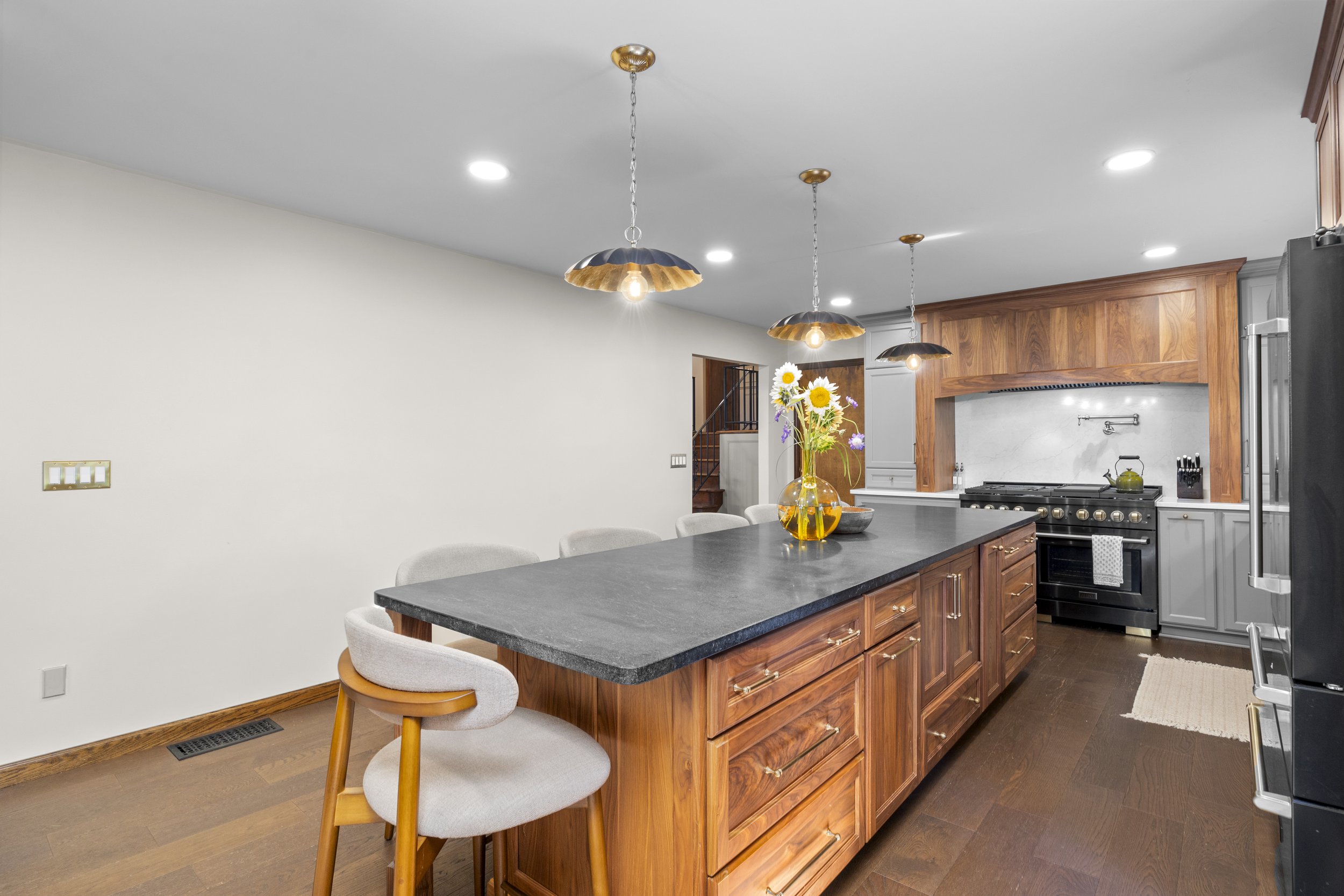 Modern kitchen with wooden cabinets, black countertop island, stainless steel appliances, and a vase with daisies on the island, illuminated by three hanging pendant lights with scalloped edges.