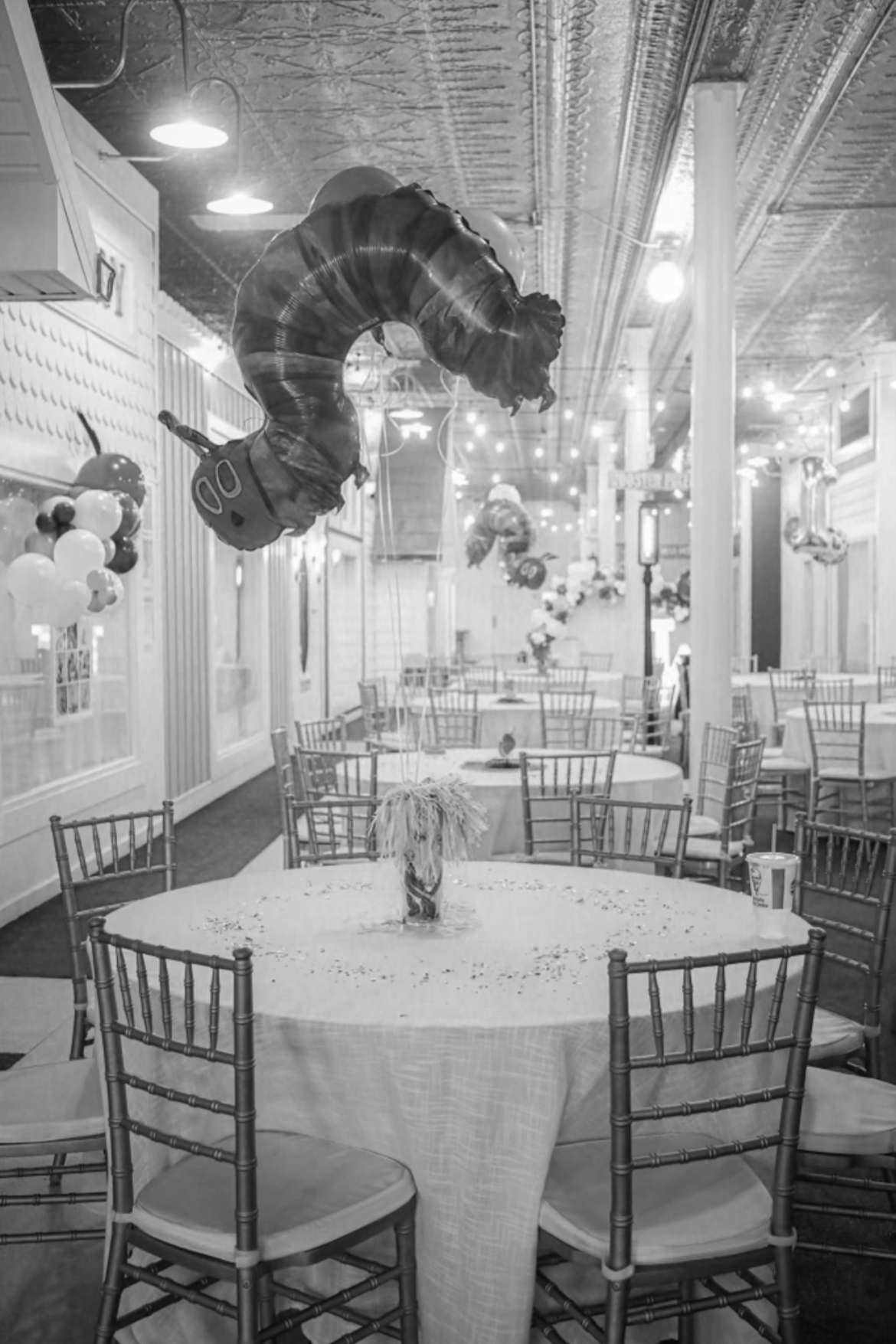 Decorated party room with balloons; chairs and tables, one with a dog cake on it, and balloon decorations hanging from ceiling.