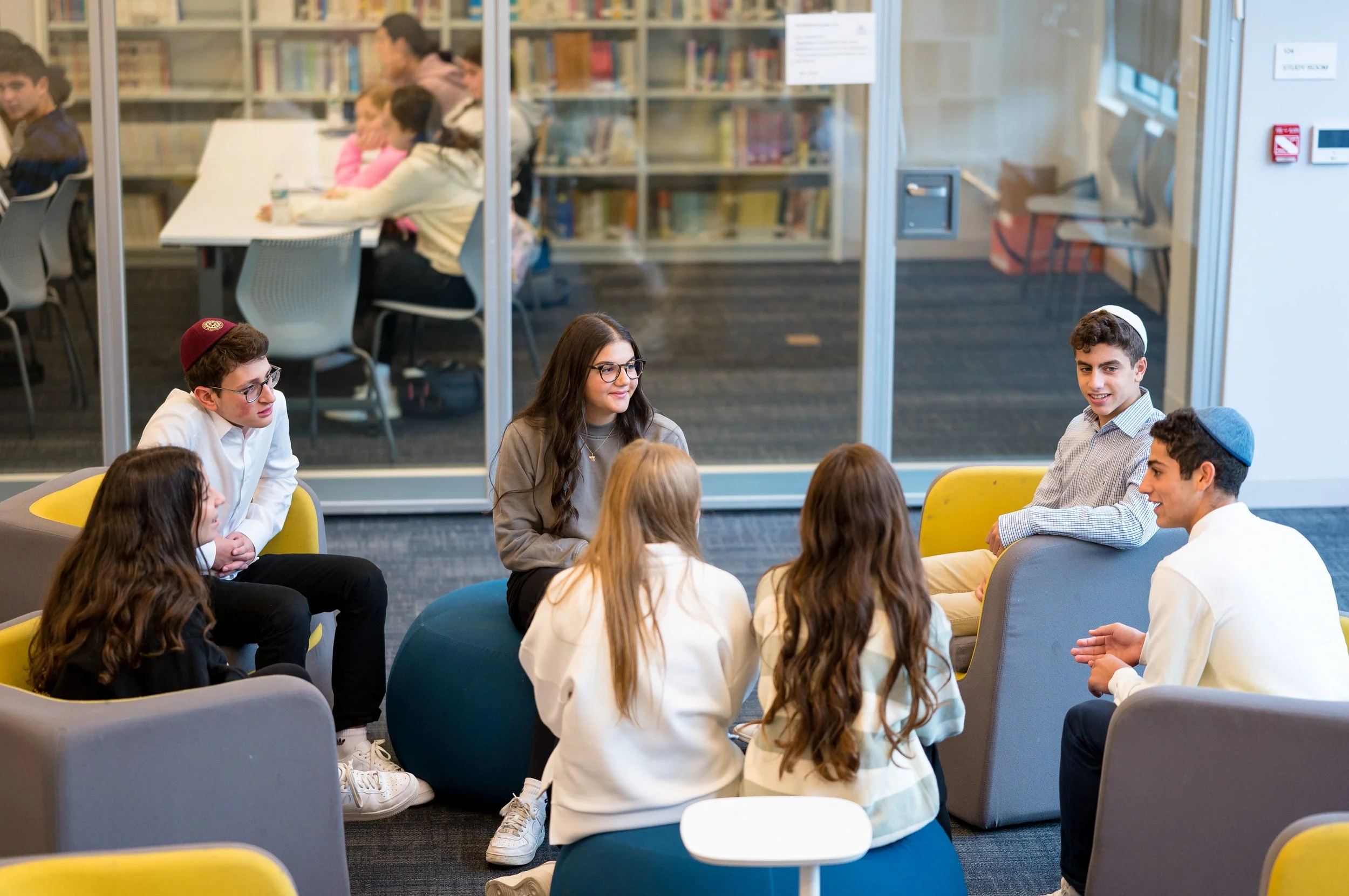 Group of young people sitting in a circle engaged in conversation in a modern library or study space.