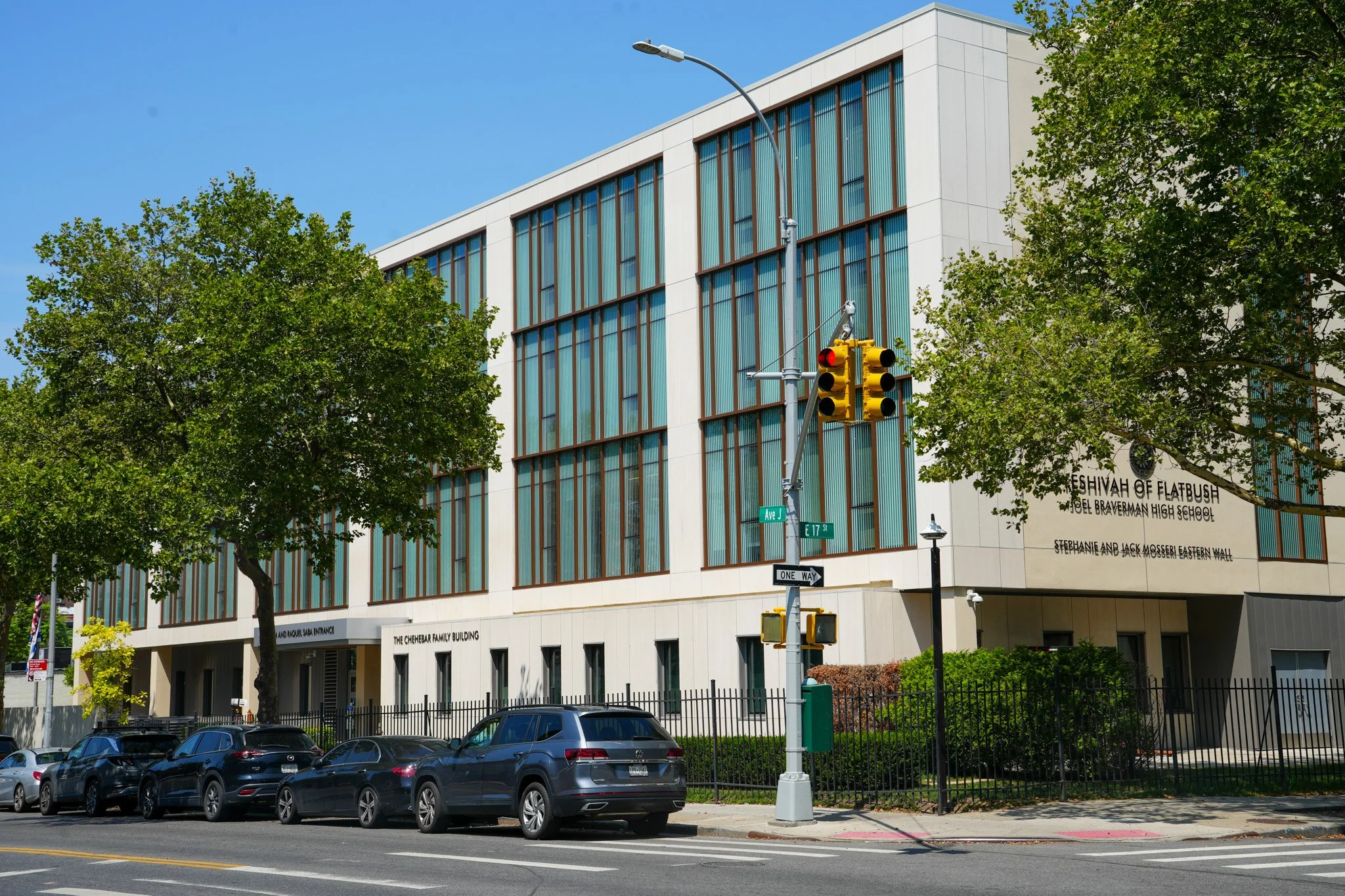 Street view of a modern building with large glass windows, trees, a traffic light, and parked cars, in an urban area. The building's signage indicates it is the Chehebar Family Building.