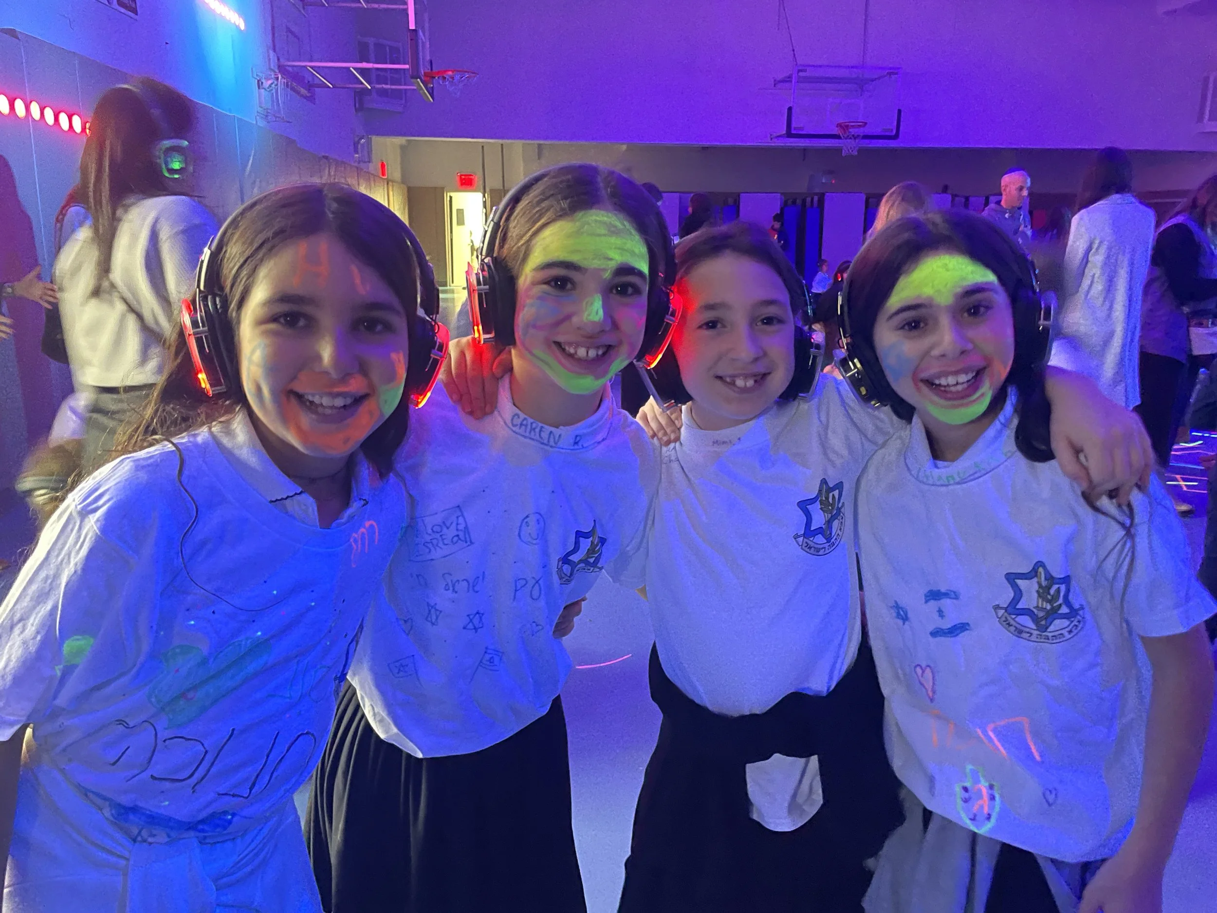 Group of children with face paint and headsets at a glow-in-the-dark event in a gymnasium.