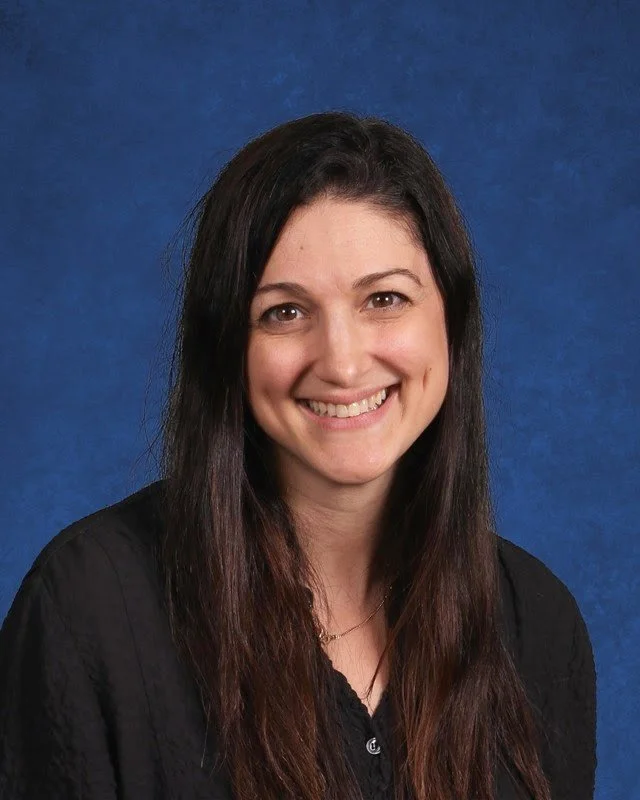 A woman with long dark hair, smiling, wearing a black top, against a blue background.