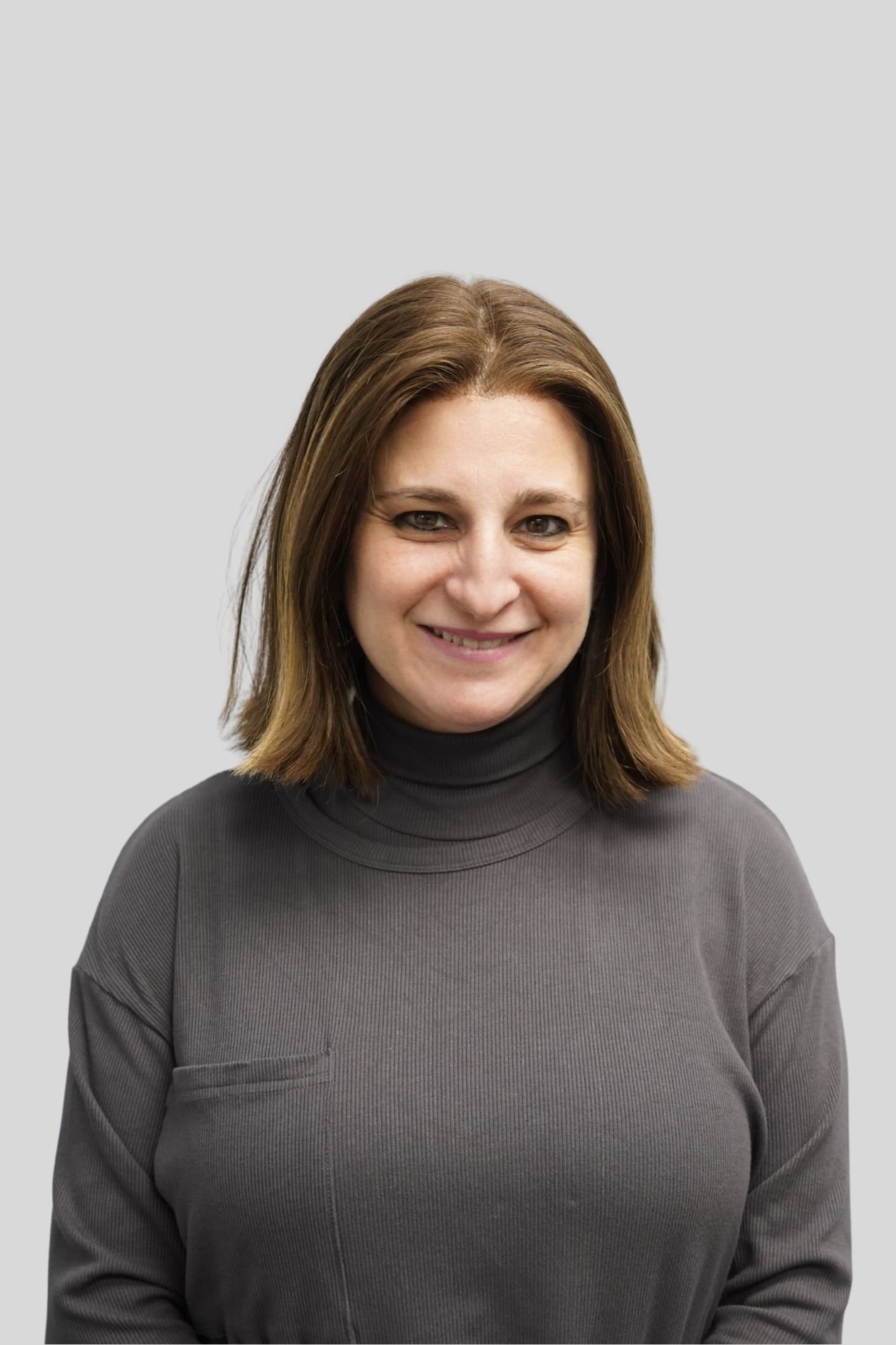 Portrait of a woman with shoulder-length brown hair, wearing a dark turtleneck sweater, smiling against a plain light gray background.