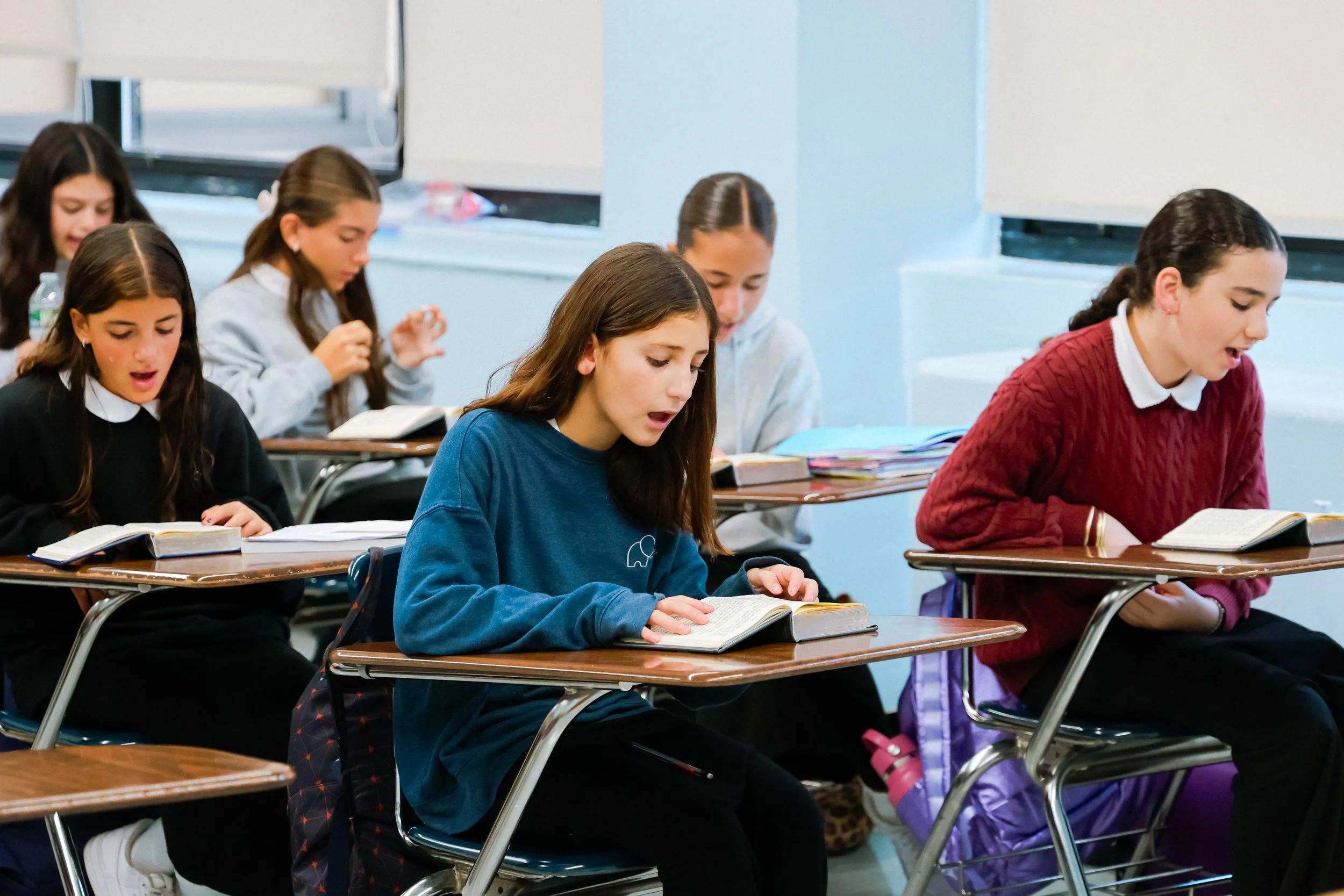 Students sitting at desks in a classroom, reading books and engaged in study.